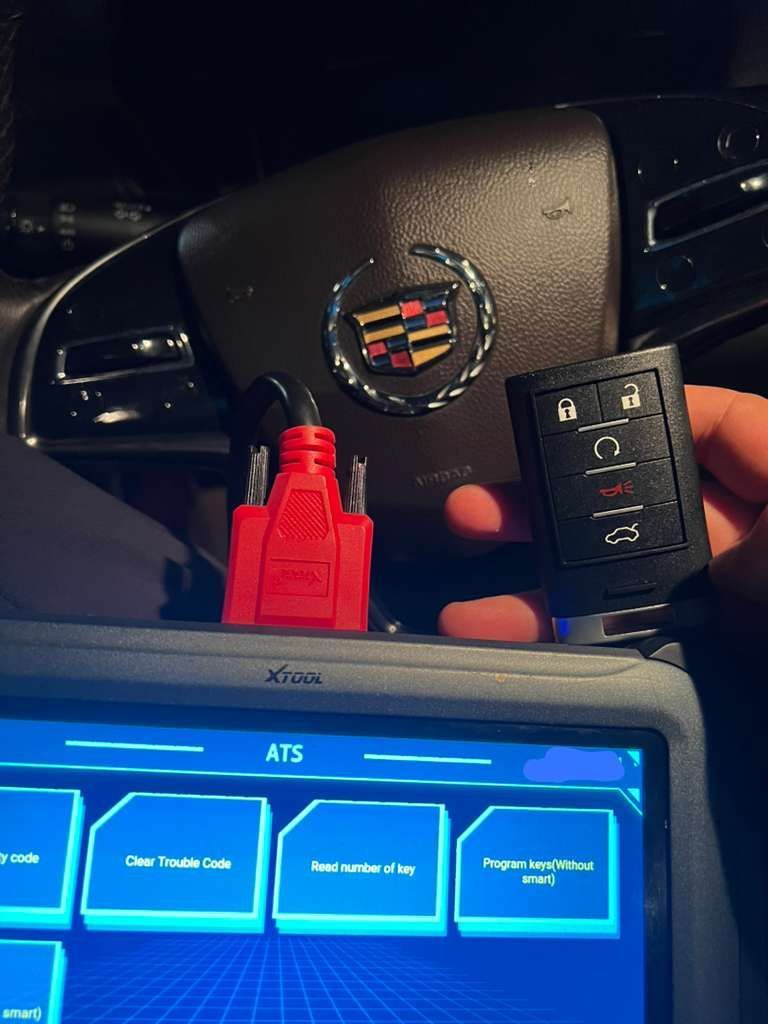 Diagnostic tool next to a Cadillac steering wheel and key fob, likely for vehicle troubleshooting.