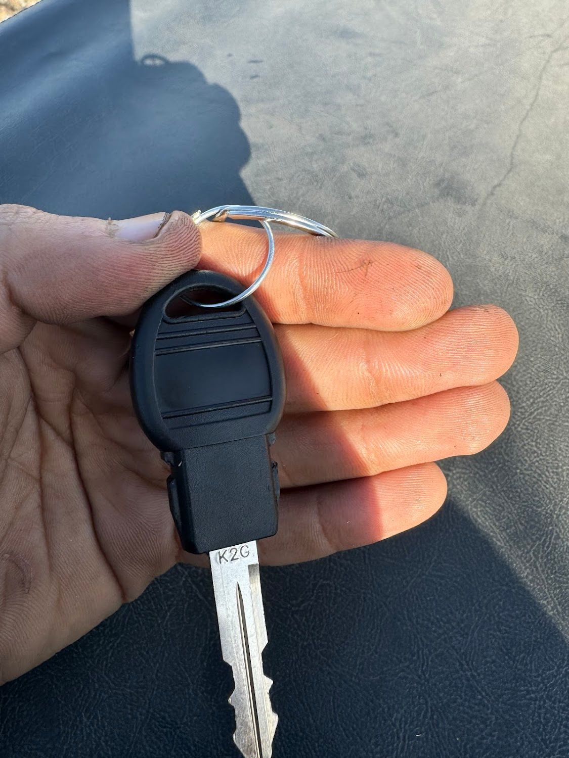 Hand holding a black car key with a metal key ring against a dark background.