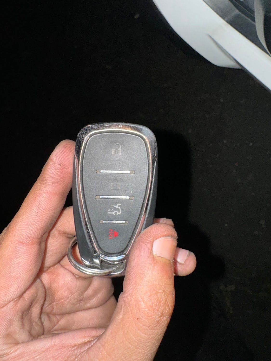 Hand holding a car key fob with buttons, including lock, unlock, and panic, with a red light on.