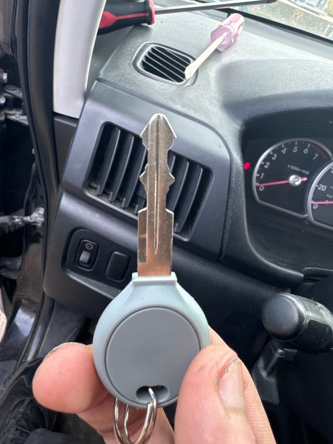A person holding a car key in front of a car dashboard with a screwdriver.