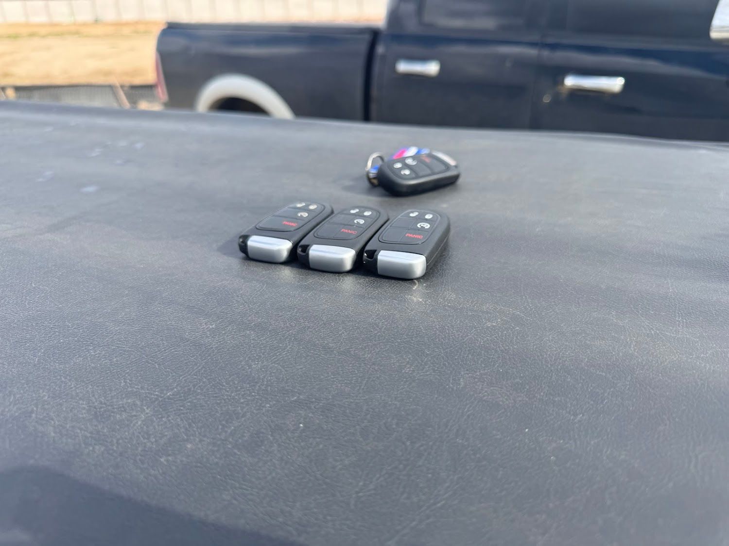 Four car keys on a black truck bed.