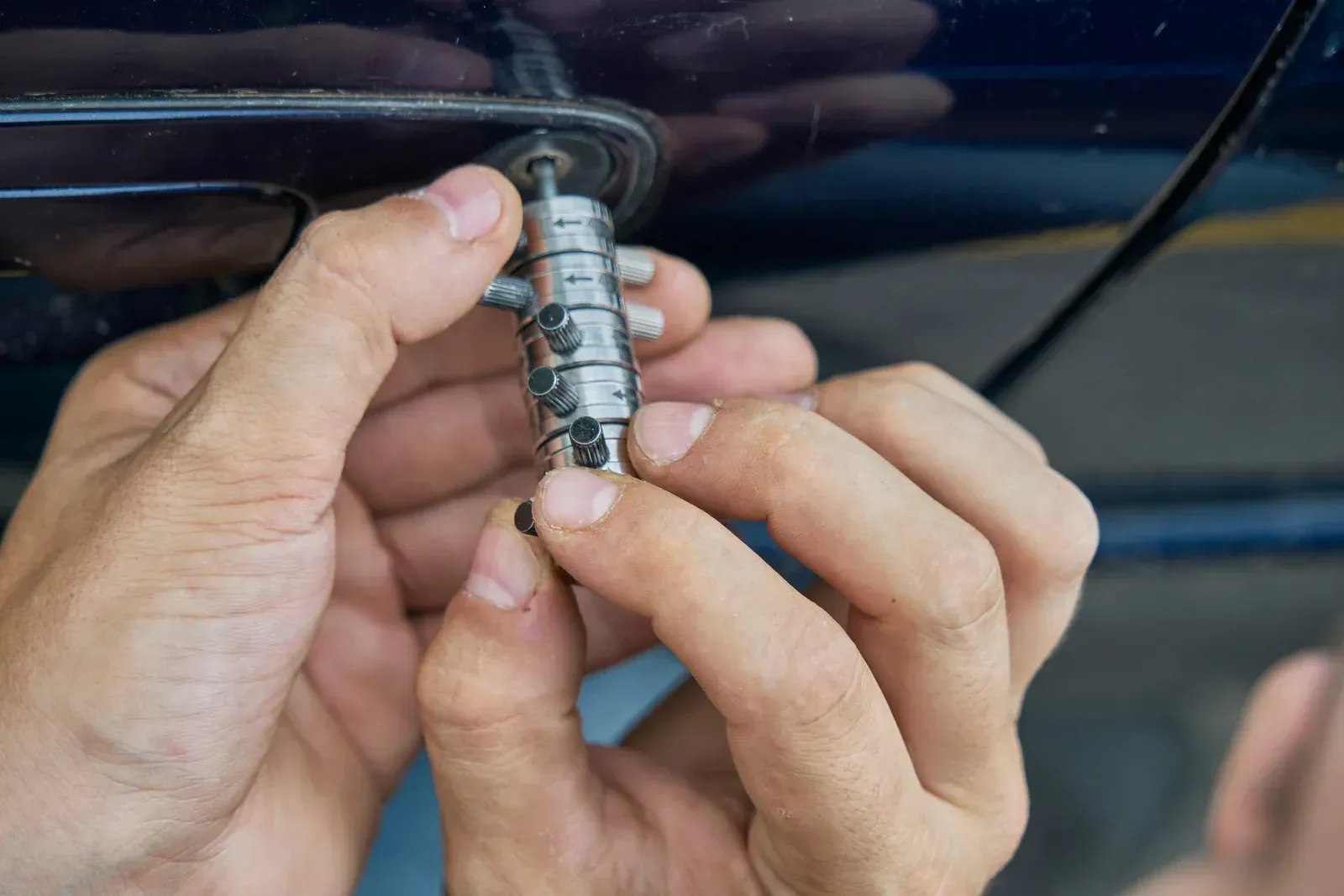 Hands removing or assembling a car door lock cylinder; blue car in the background.