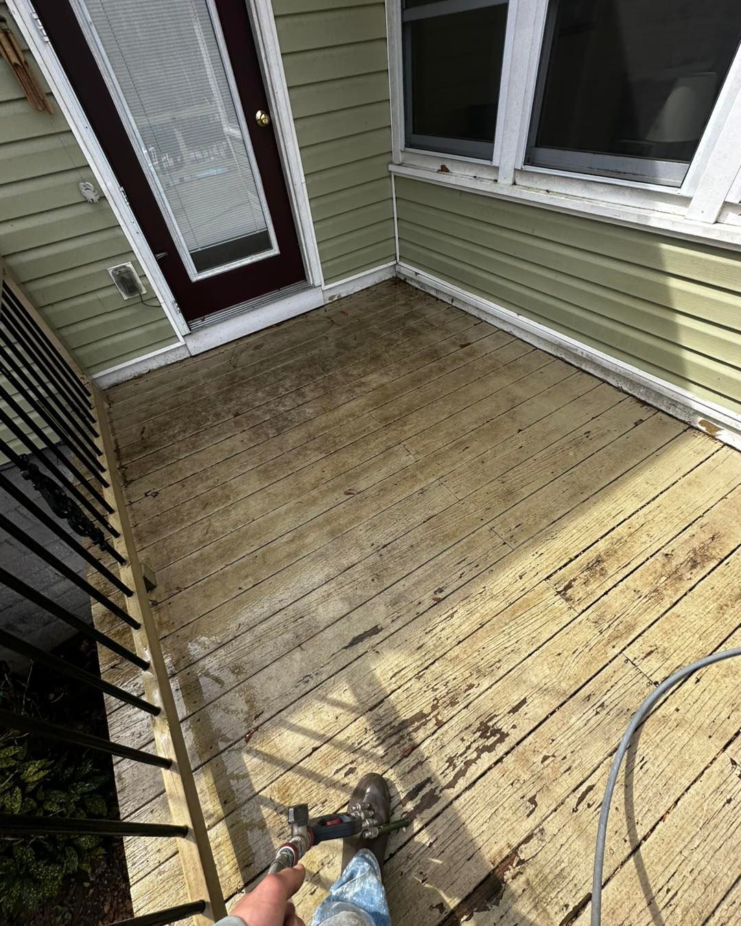 A person is cleaning a wooden deck with a hose.