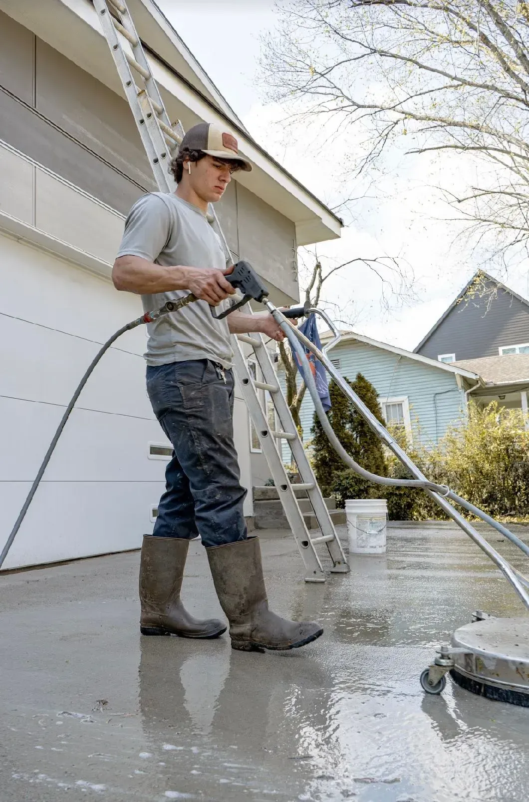 A man is cleaning the driveway of a house with a pressure washer.