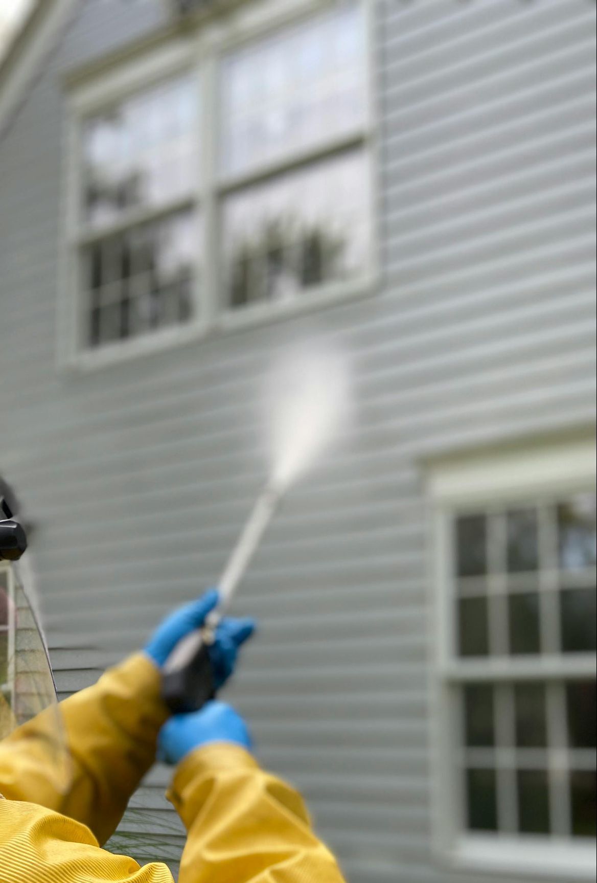 A man in a yellow jacket is using a high pressure washer to clean a house