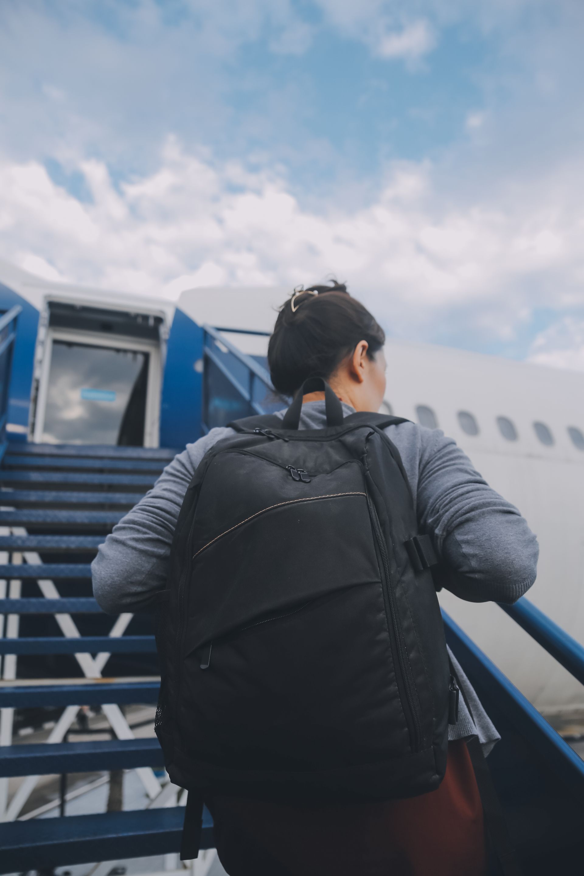 A man with a backpack is walking up the stairs to an airplane.