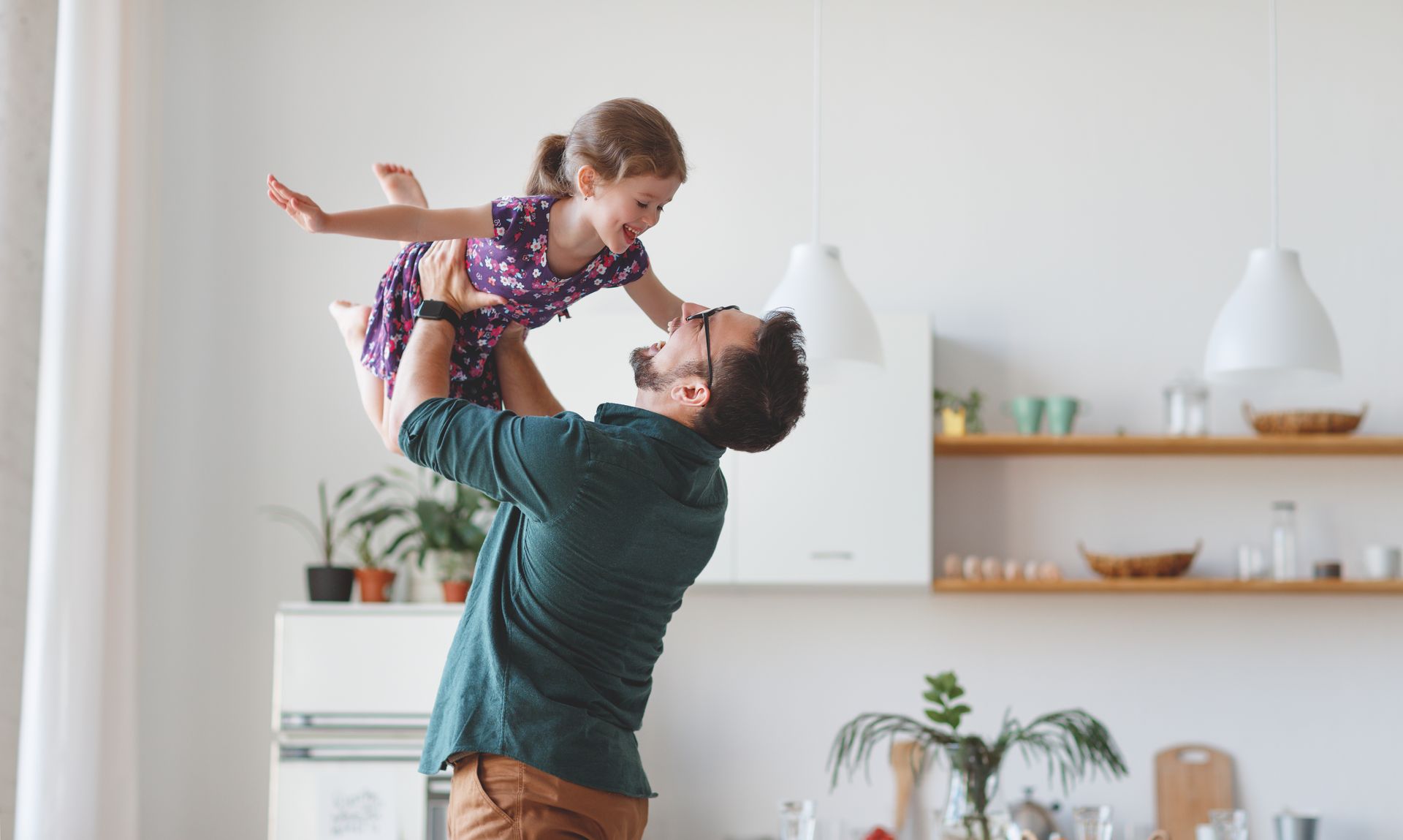 Man lifting a smiling child indoors in a bright, modern kitchen