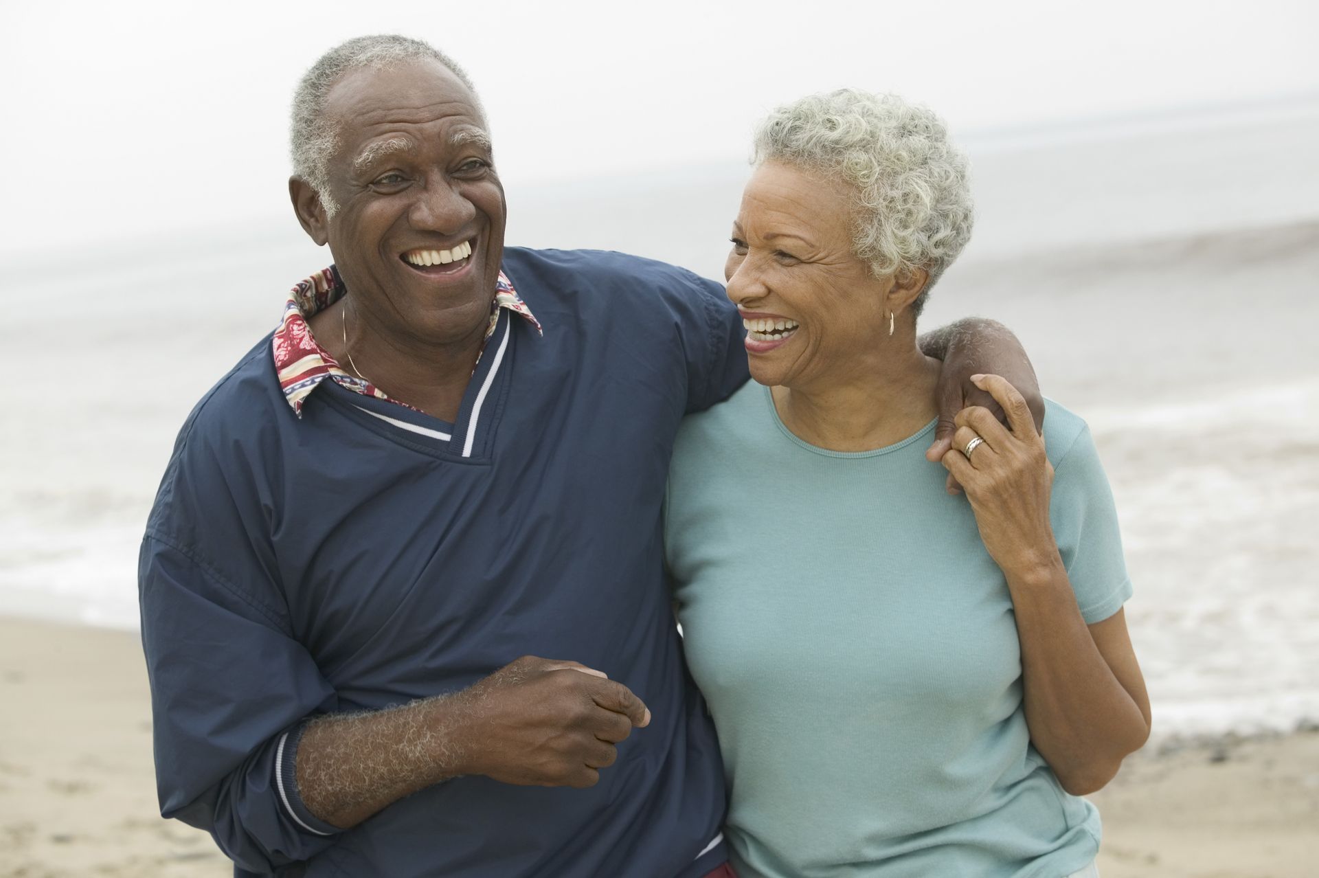 Two people smiling and walking arm in arm on a beach with waves in the background