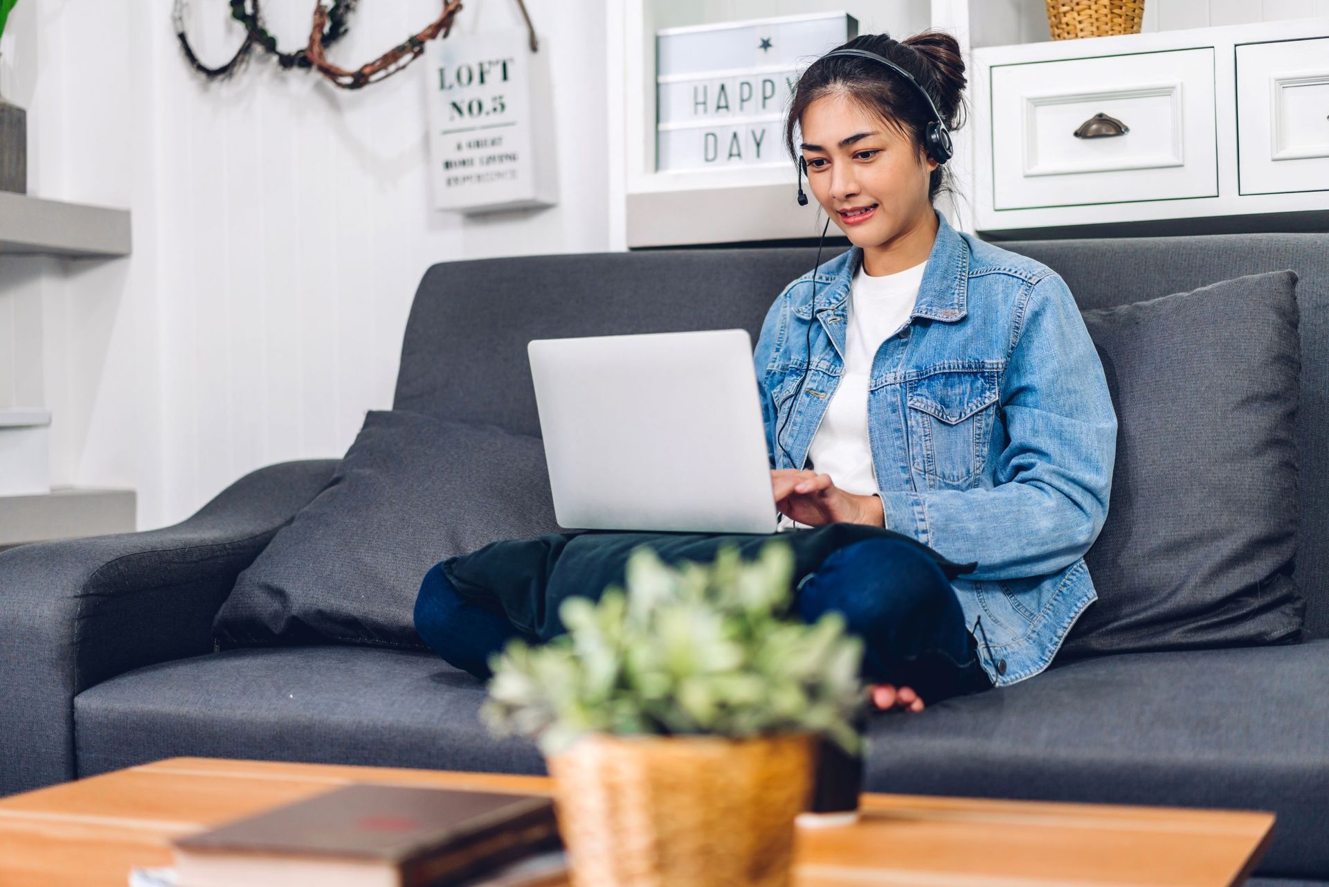 Woman using a laptop on a dark gray couch in a bright living room