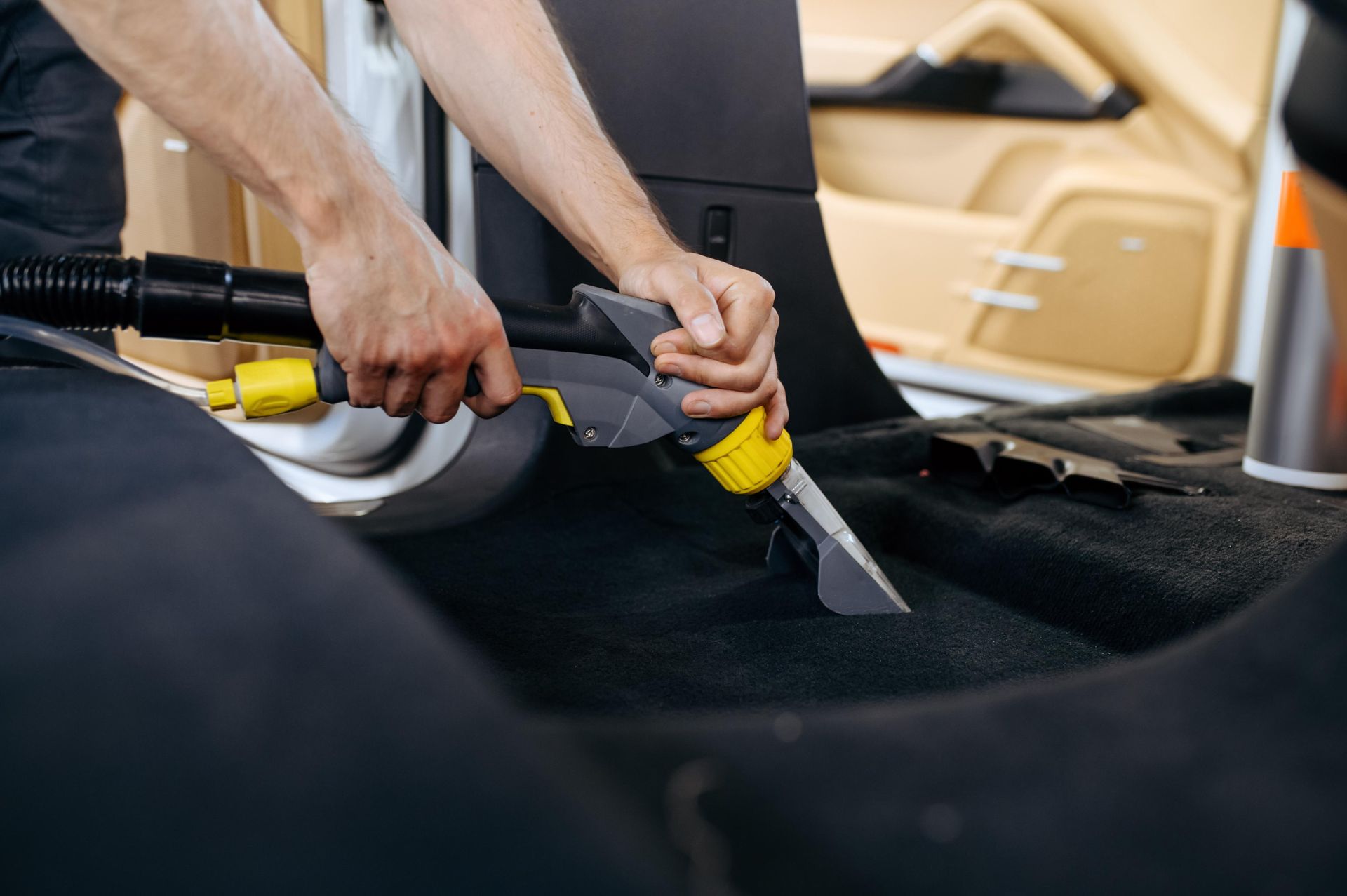 Person vacuuming car interior with a handheld vacuum, black carpet.