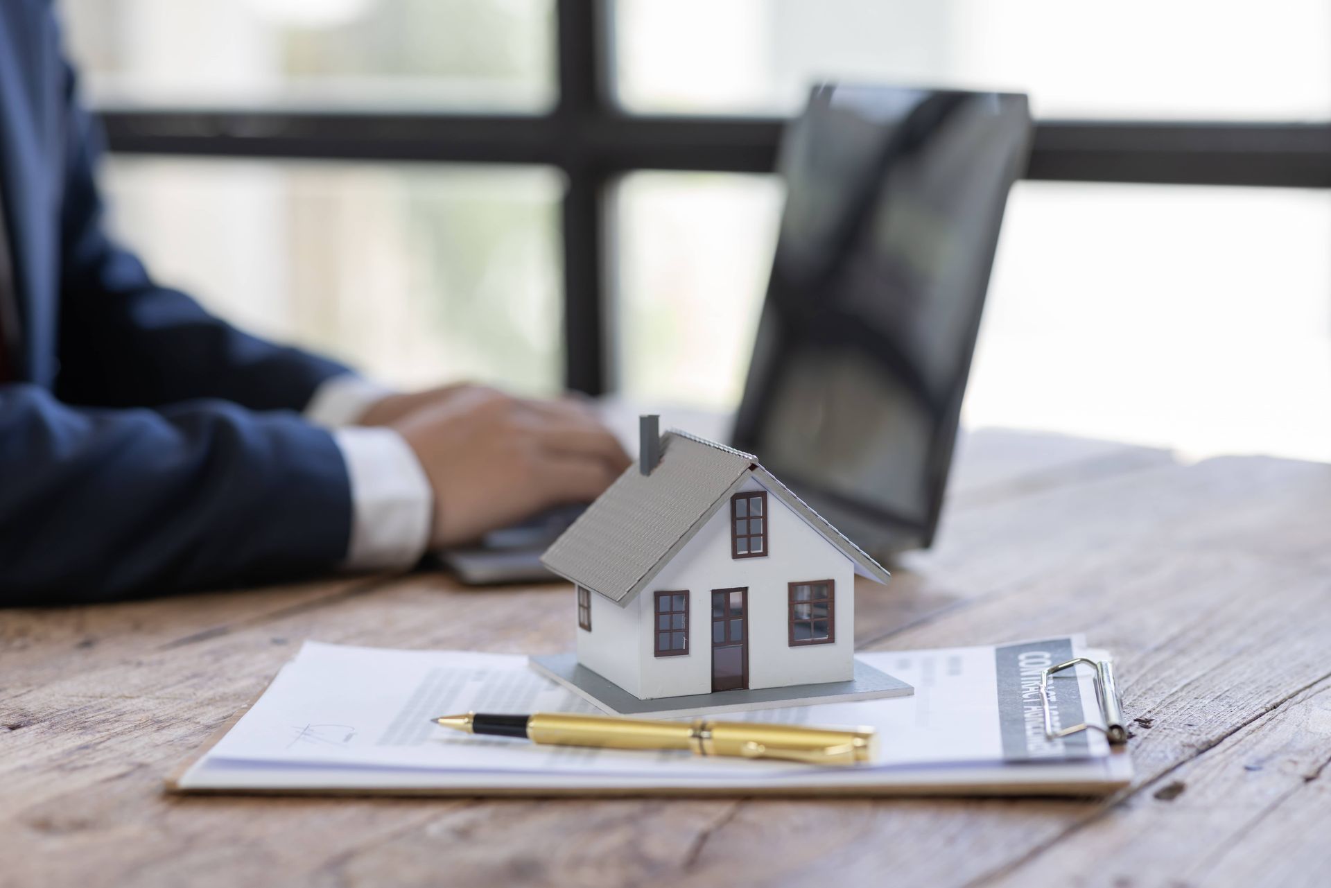 A man is sitting at a desk with a laptop and a model house.