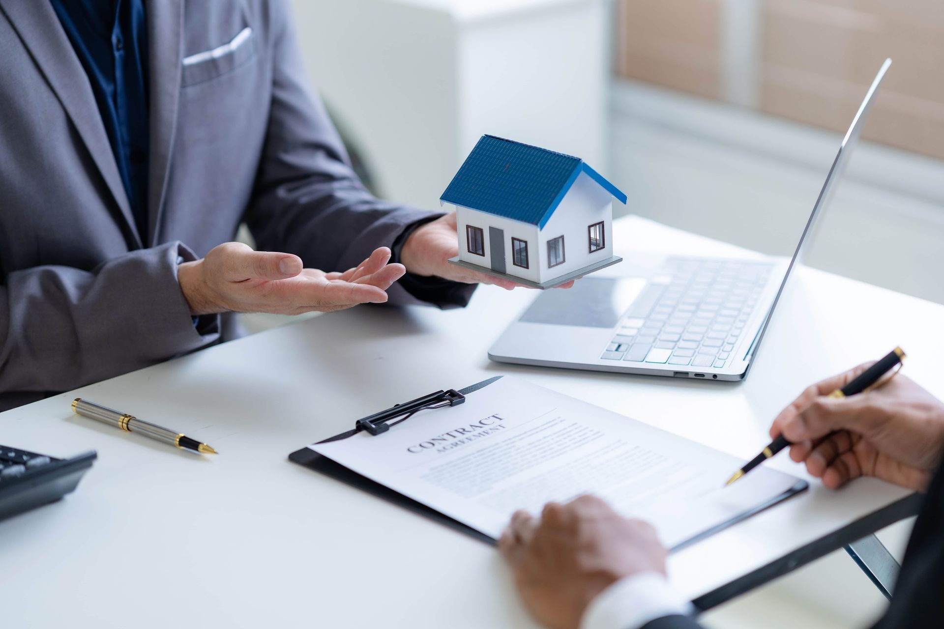 A woman is holding a model house in her hand while a man is signing a contract.
