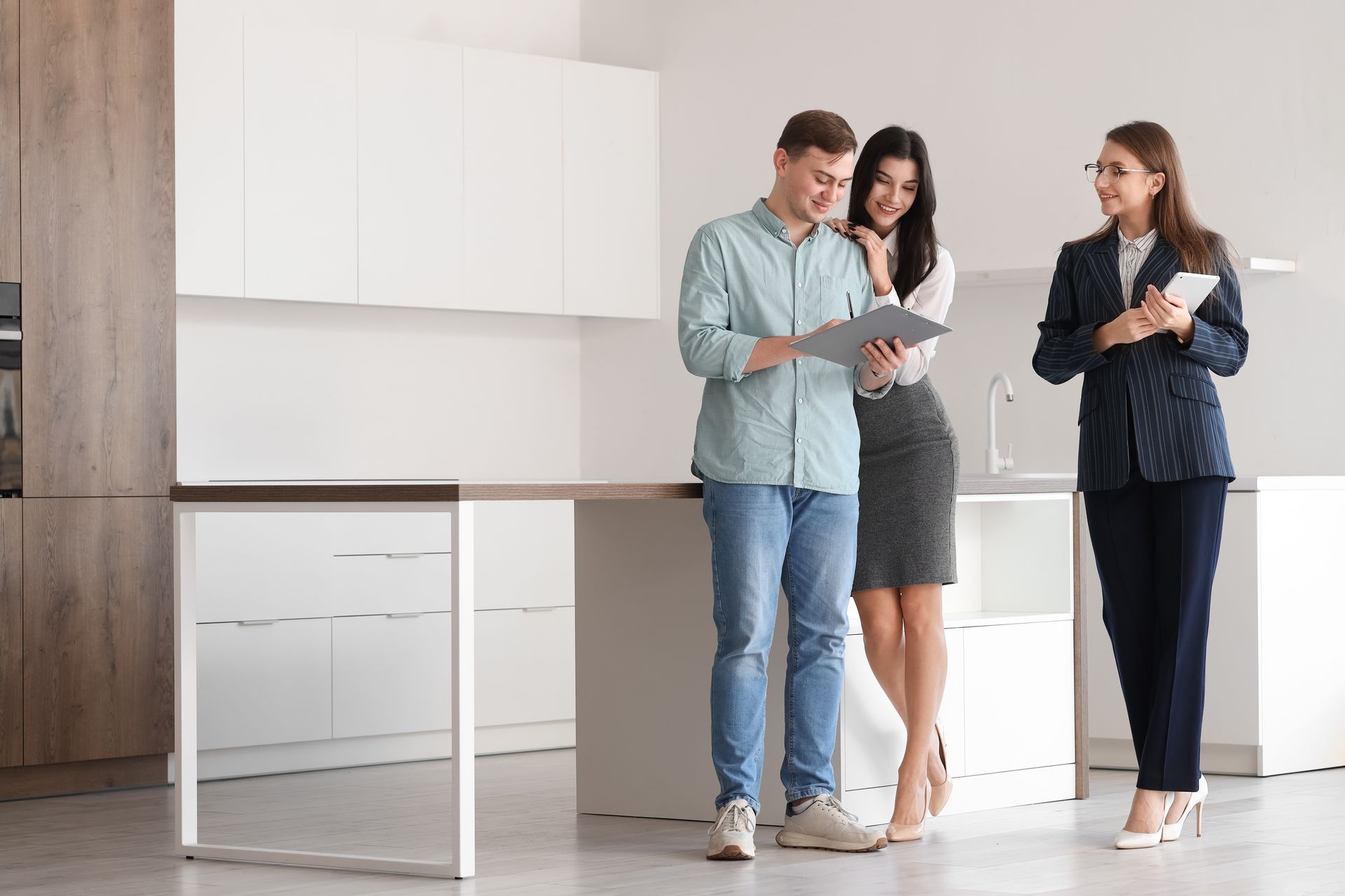 A man and a woman are standing in a kitchen with a real estate agent.