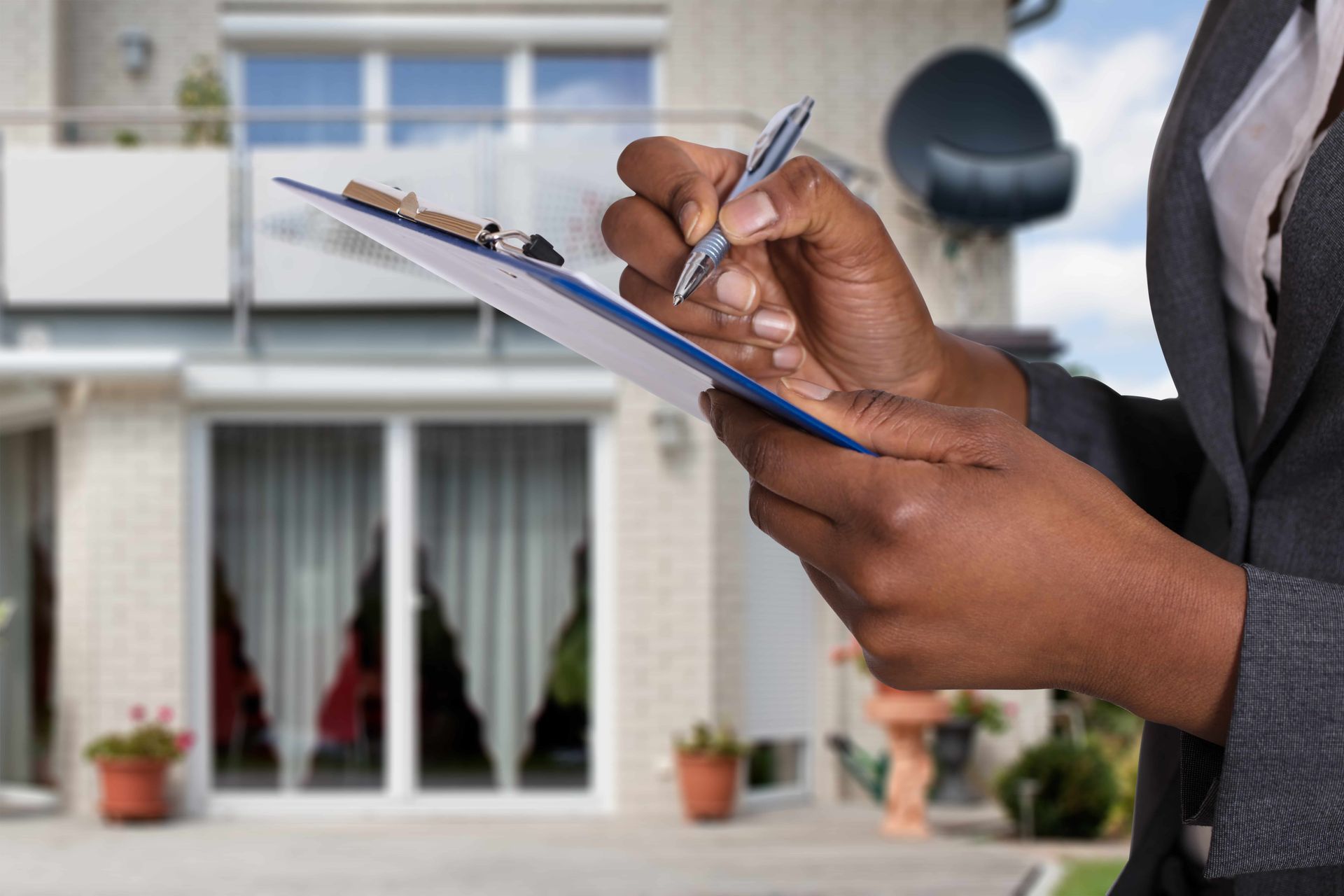 A woman is writing on a clipboard in front of a house.