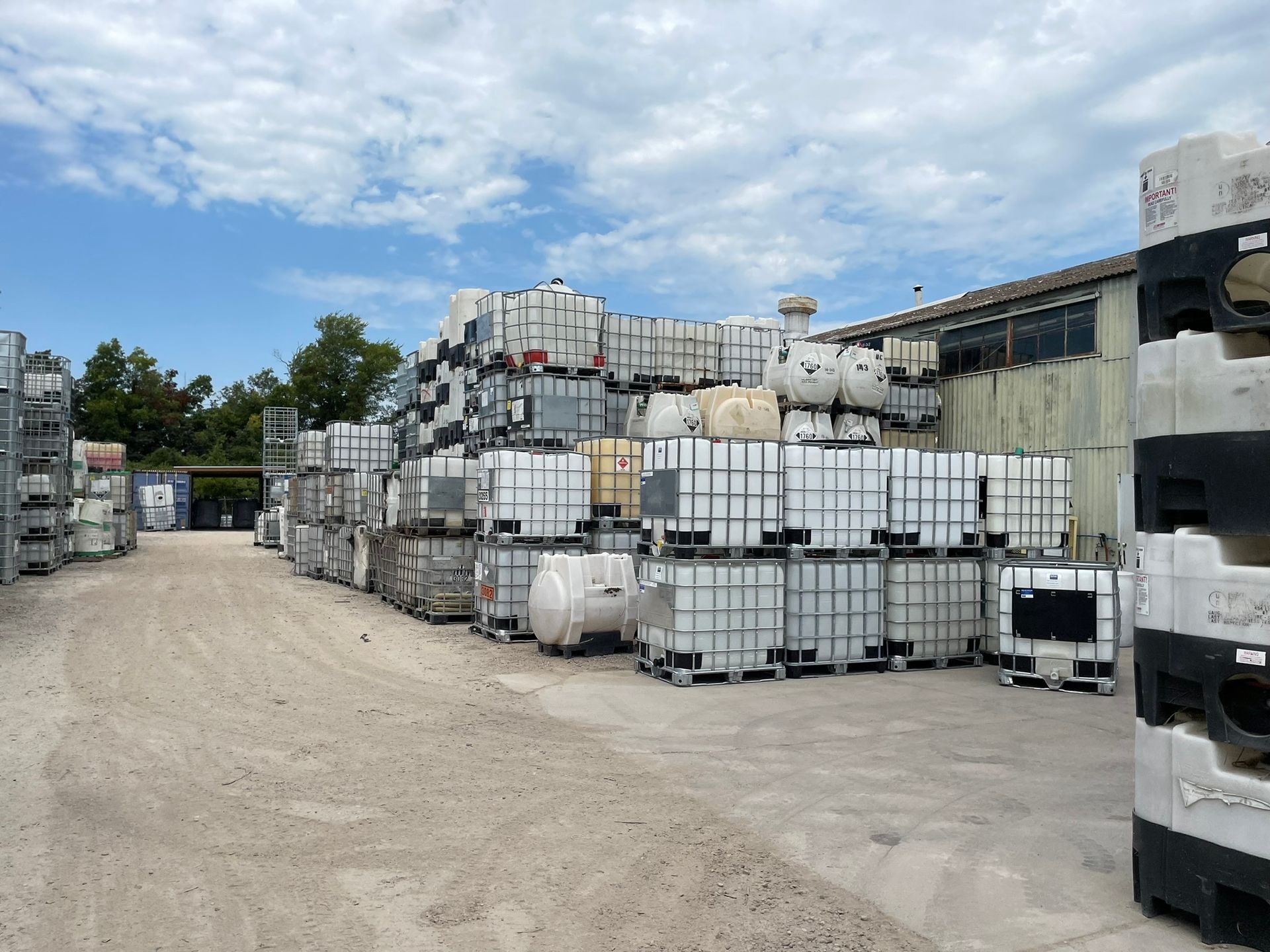 Outdoor storage yard with stacks of white industrial containers under a cloudy sky.