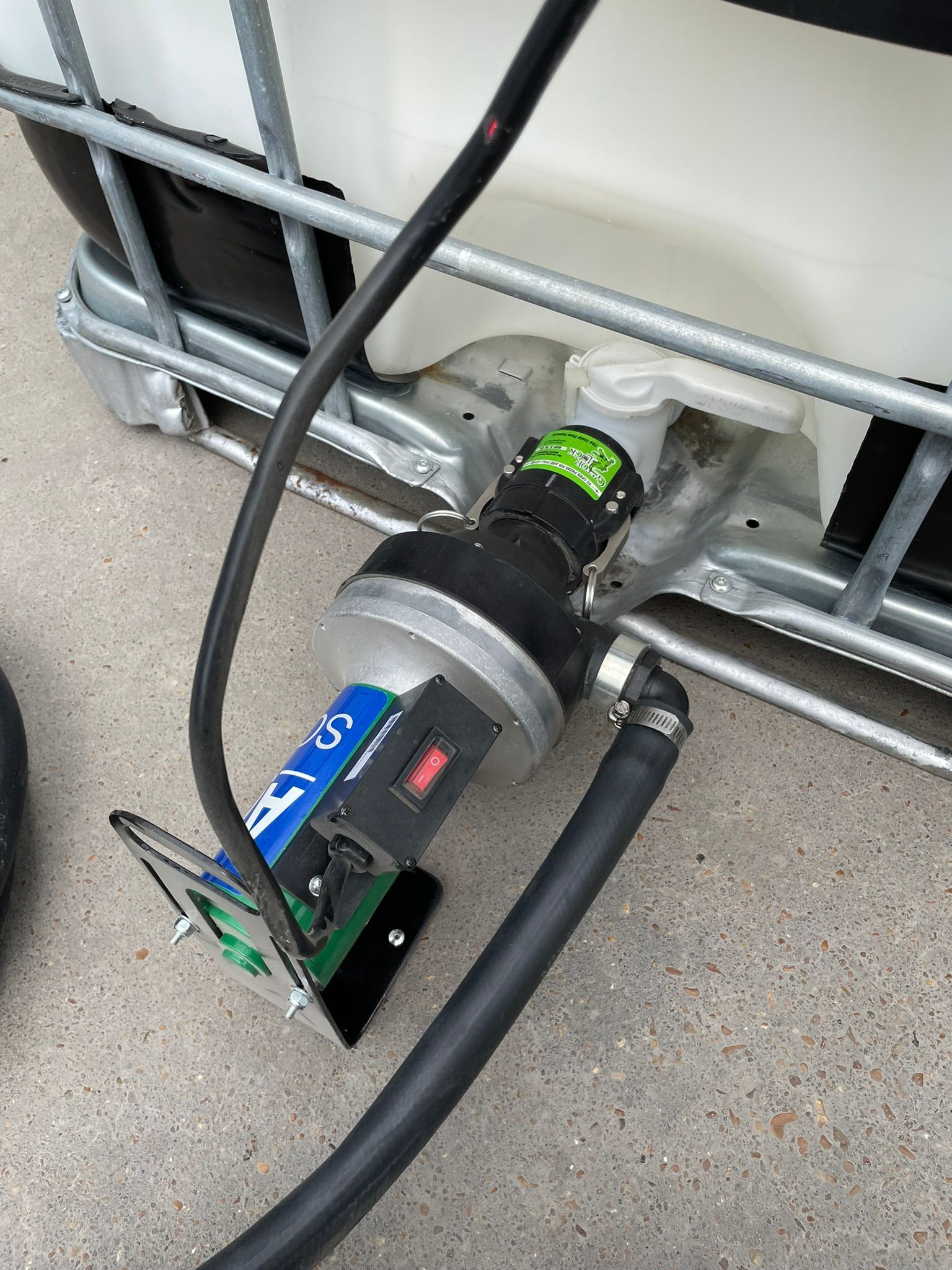 A pump connected to a large white tank with a black hose and electrical components.
