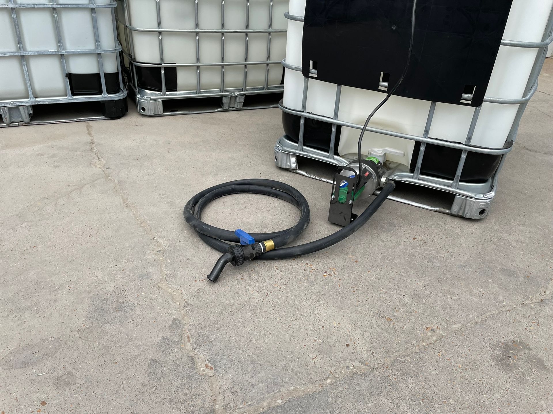 Three industrial tanks with a pump and hose on a concrete surface.