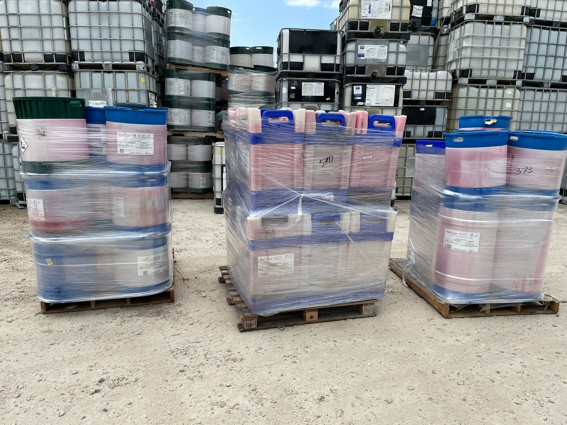Three pallets of drums wrapped in plastic, with additional containers in the background.