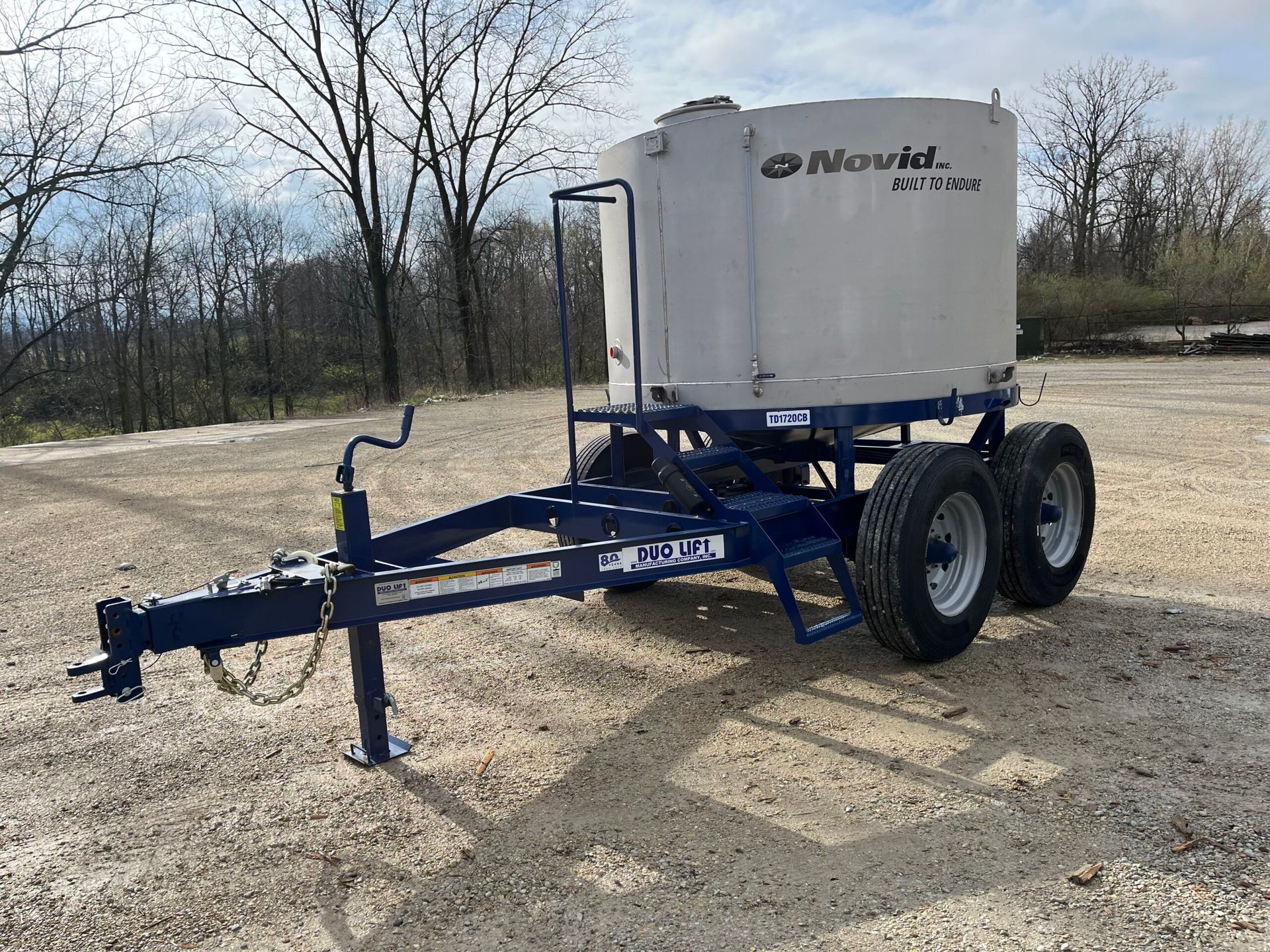 Blue and white Novid sprayer trailer on gravel.