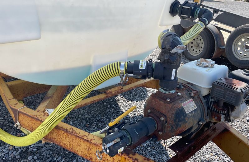 Yellow hose connected to a water tank with a pump on a trailer.
