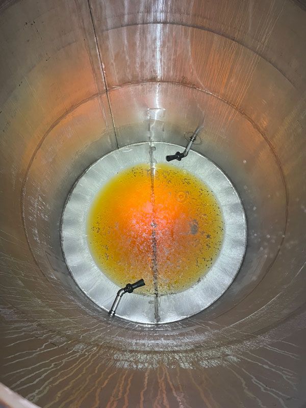 Looking down into a large, metal tank with a yellow-orange liquid at the bottom and probes extending into the liquid.