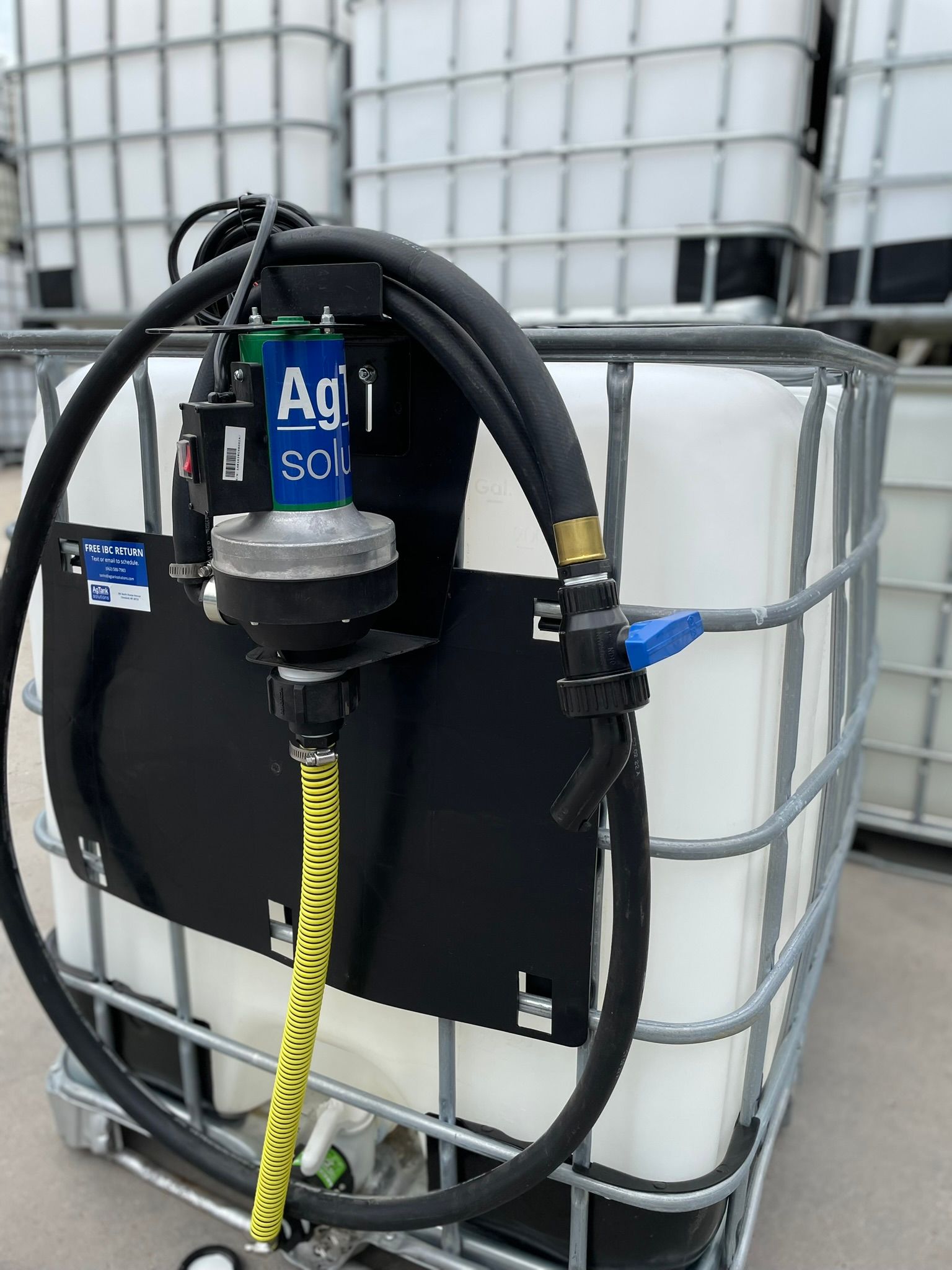 A tank with a pump and hose, inside a metal cage, with an AgSol label attached.