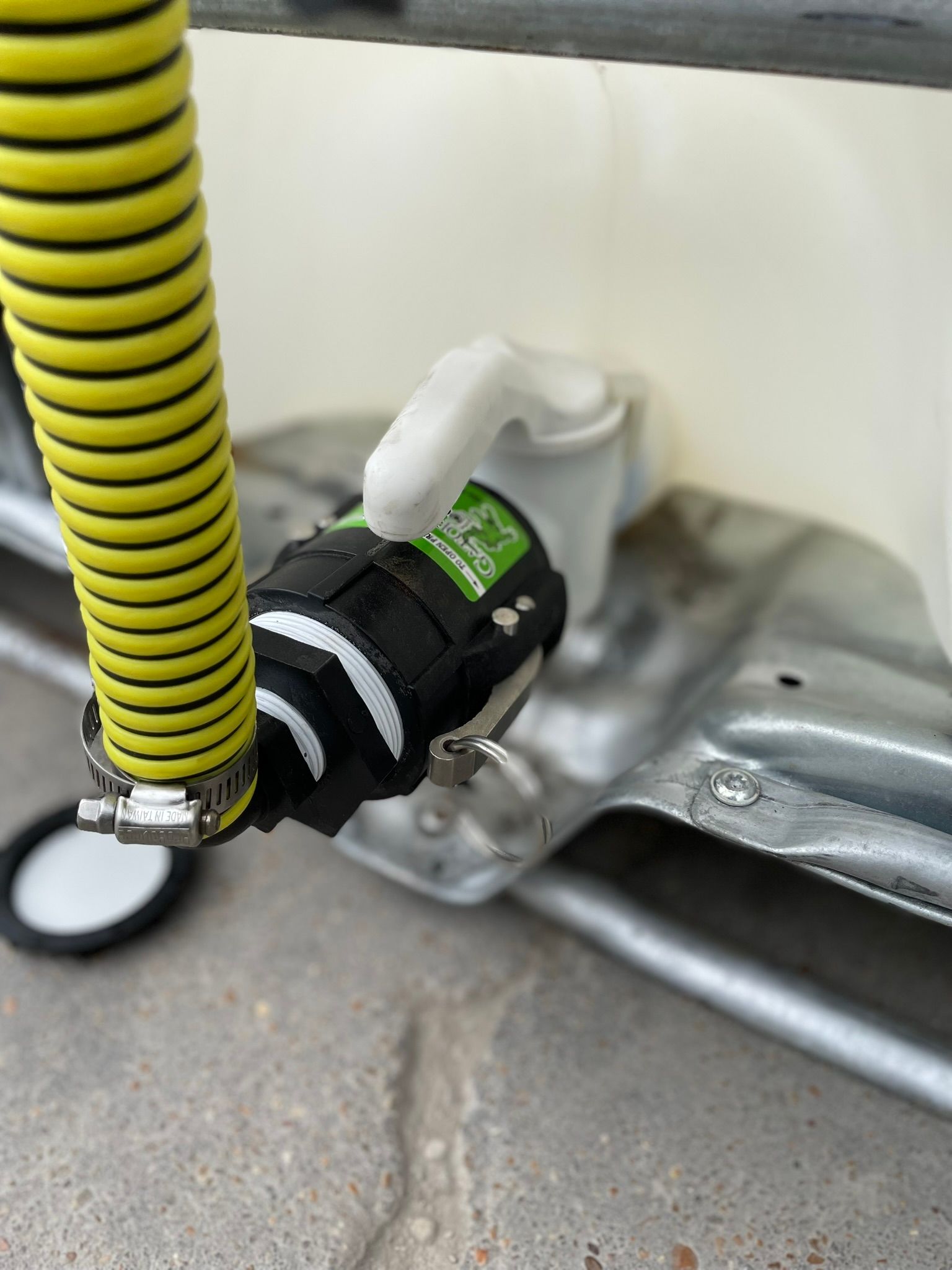 Close-up of a tank outlet with a black and white fitting, yellow hose, and white tank.