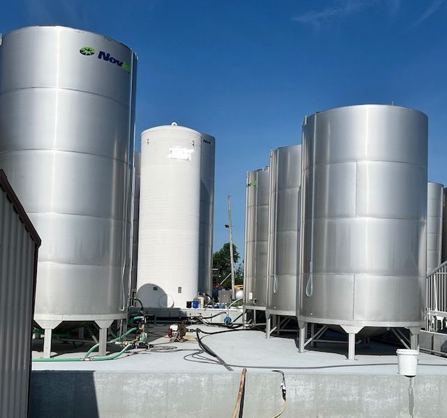 Outdoor view of multiple stainless steel industrial storage tanks on a concrete pad under a clear blue sky.