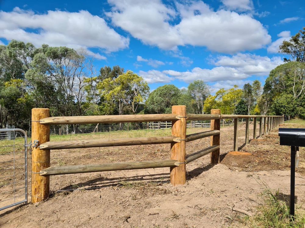 Wooden Fence With Gate in a Field Under a Blue Sky With Clouds — Sweet's Rural Fencing & Machinery in Lake Macdonald, QLD
