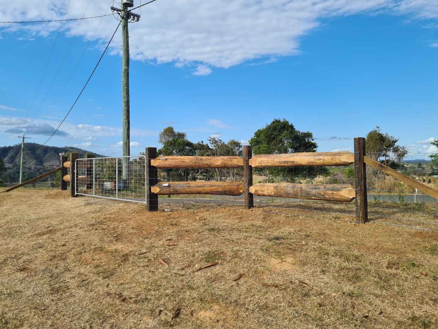 Wooden Fence with Gate on A Hilltop, Under a Blue Sky — Sweet's Rural Fencing & Machinery in Lake Macdonald, QLD