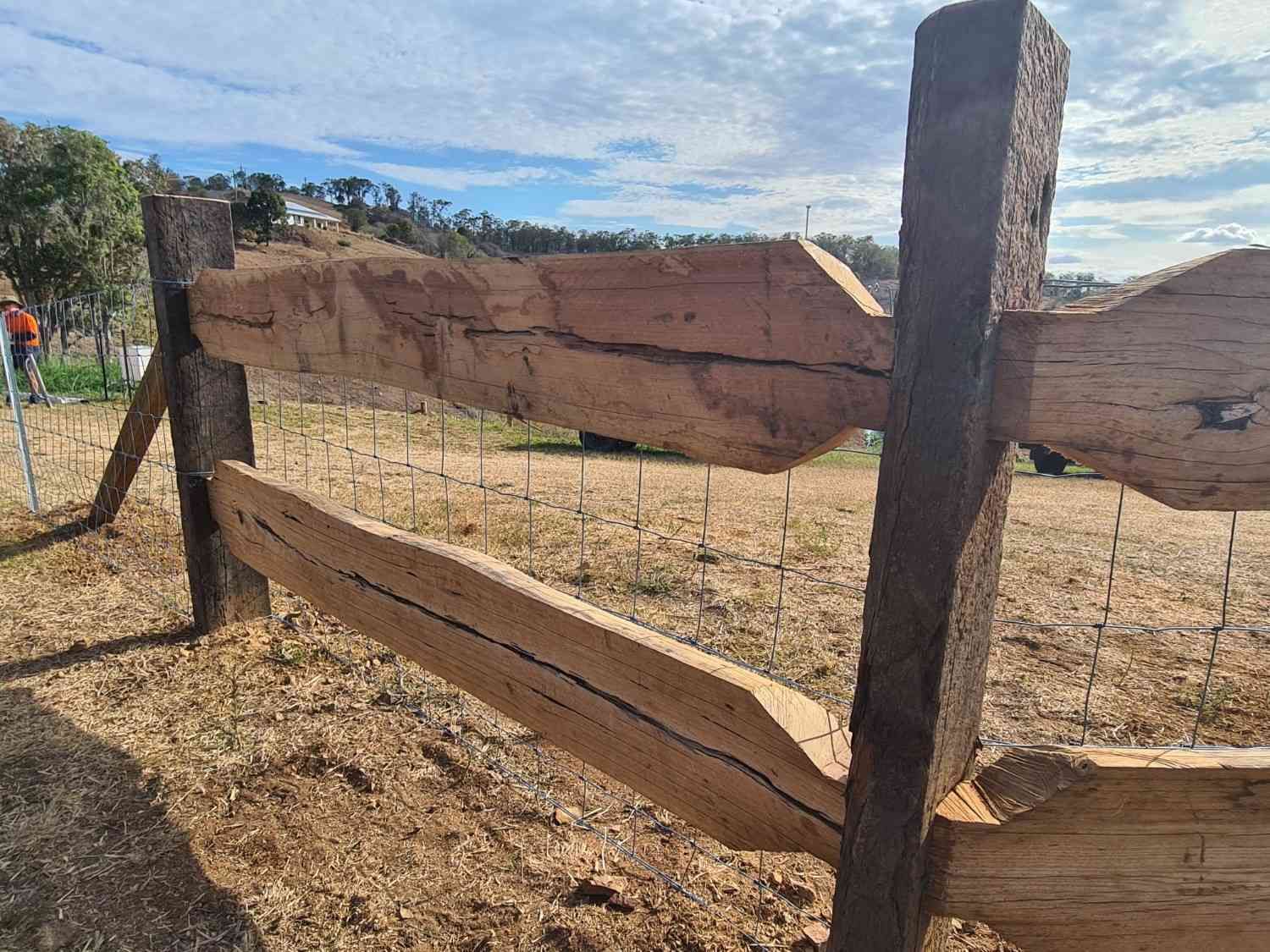 Wooden Fence with Dark, Rough-Hewn Beams in A Field — Sweet's Rural Fencing & Machinery in Lake Macdonald, QLD