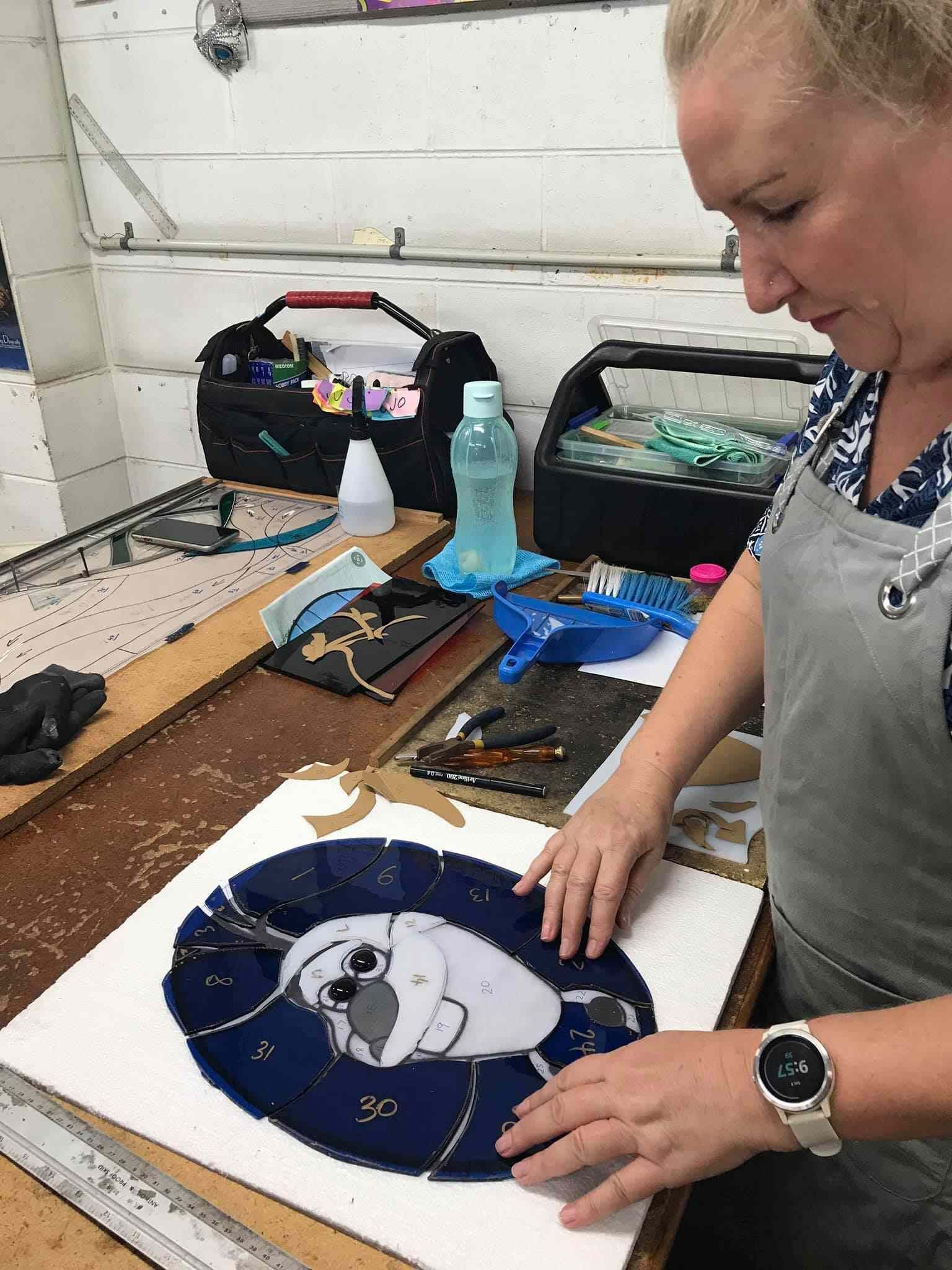 A Woman Is Sitting At A Table Making A Stained Glass Painting Of A Dog — Townsville Stained Glass In Aitkenvale, QLD
