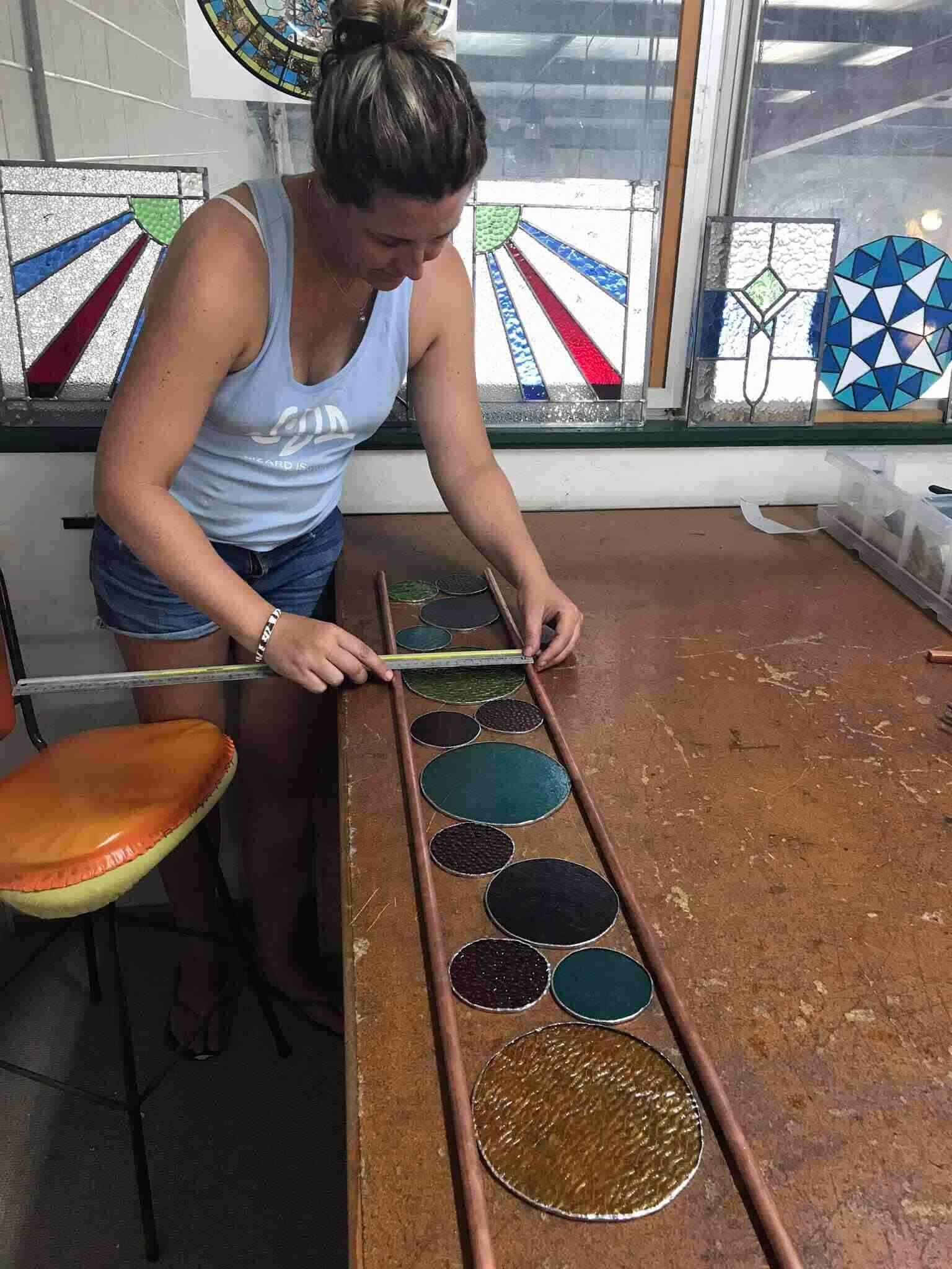 A Woman Is Measuring A Piece Of Stained Glass On A Table — Townsville Stained Glass In Aitkenvale, QLD
