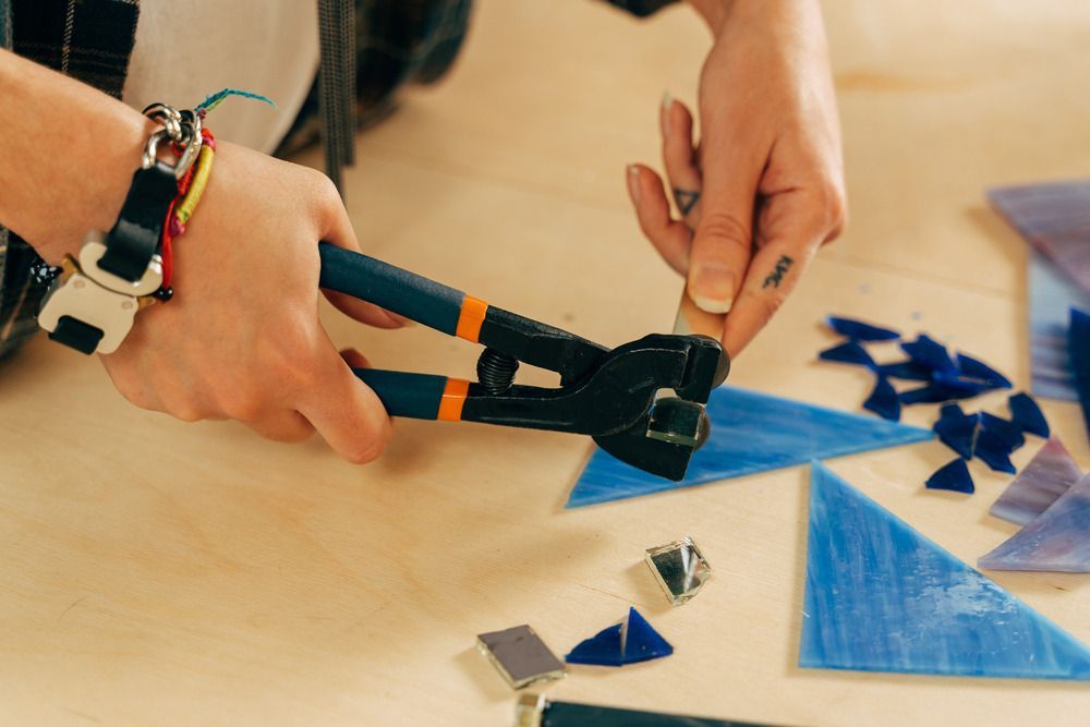 A Person Is Cutting A Piece Of Stained Glass With A Pair Of Pliers — Townsville Stained Glass In Aitkenvale, QLD