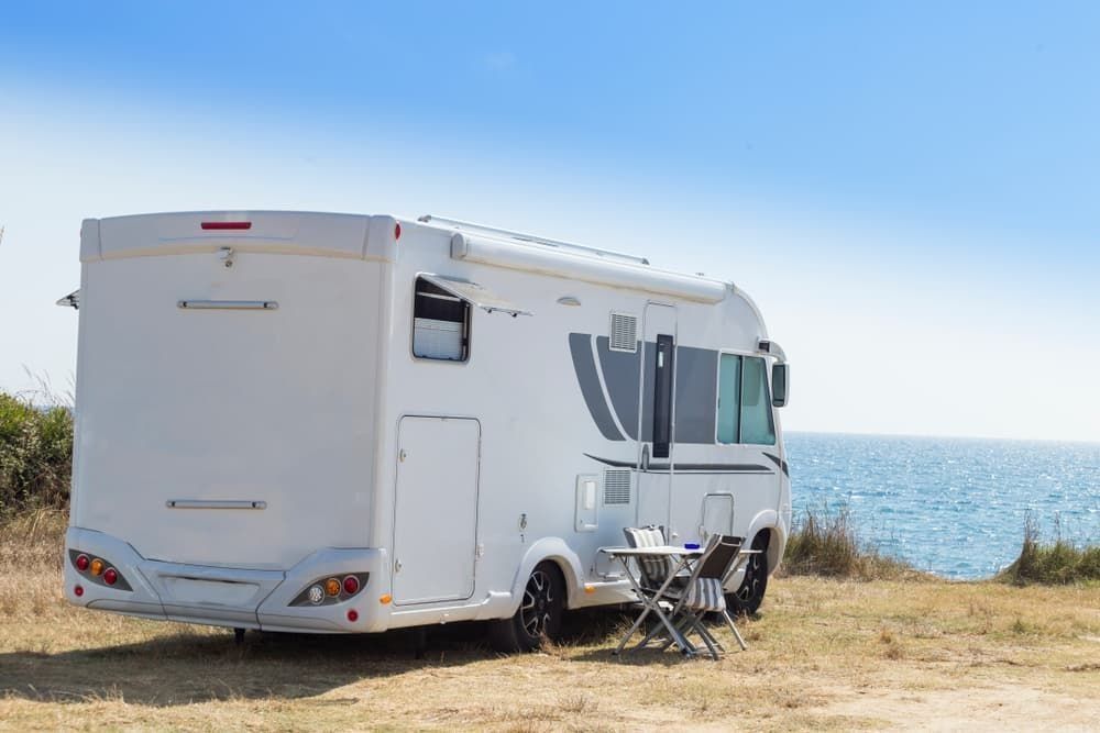 A White RV is Parked in a Field Next to the Ocean — B & C Caravan Service Pty Ltd In Dubbo, NSW