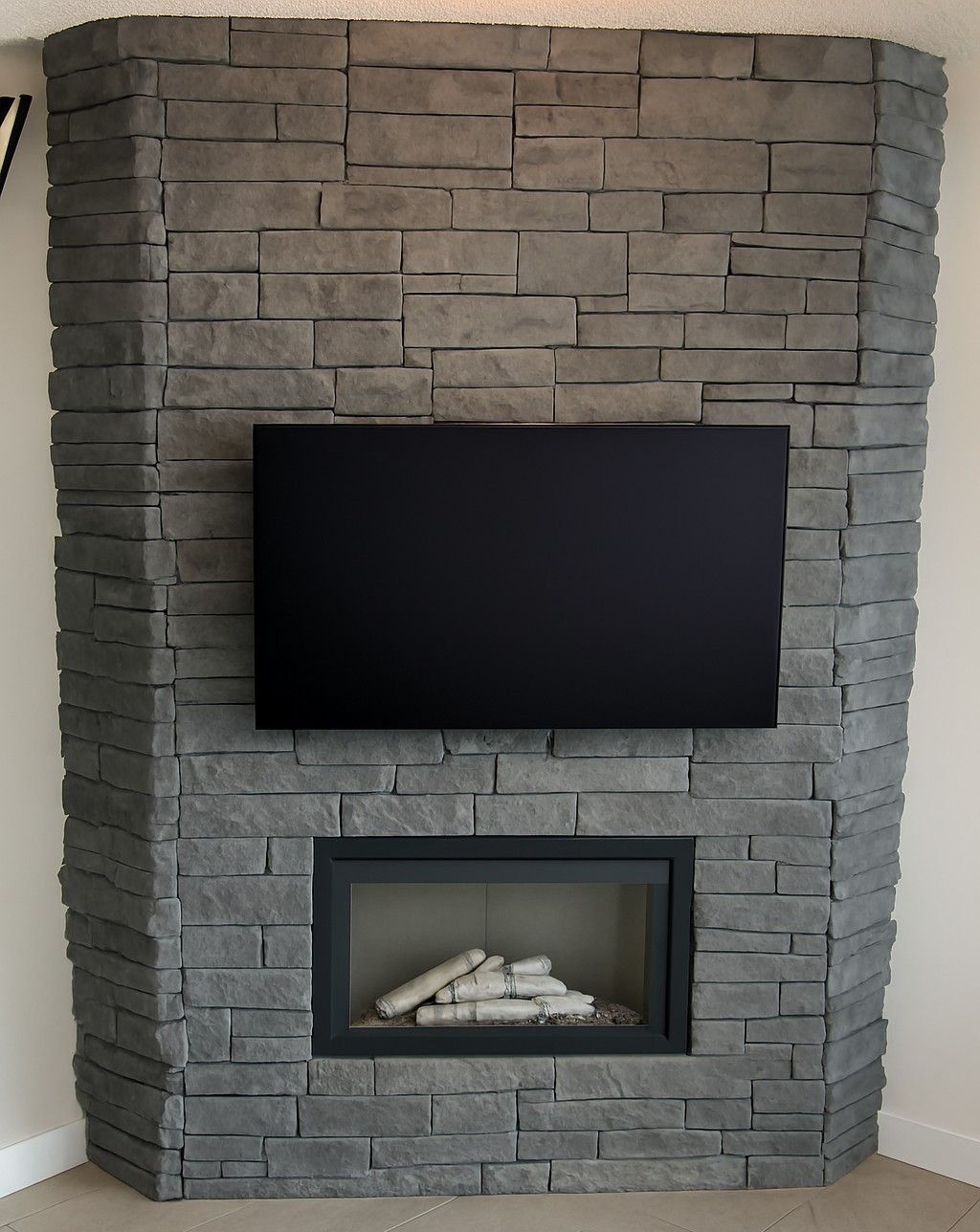 Cheminée en pierre avec un téléviseur monté au-dessus d'un foyer au gaz.