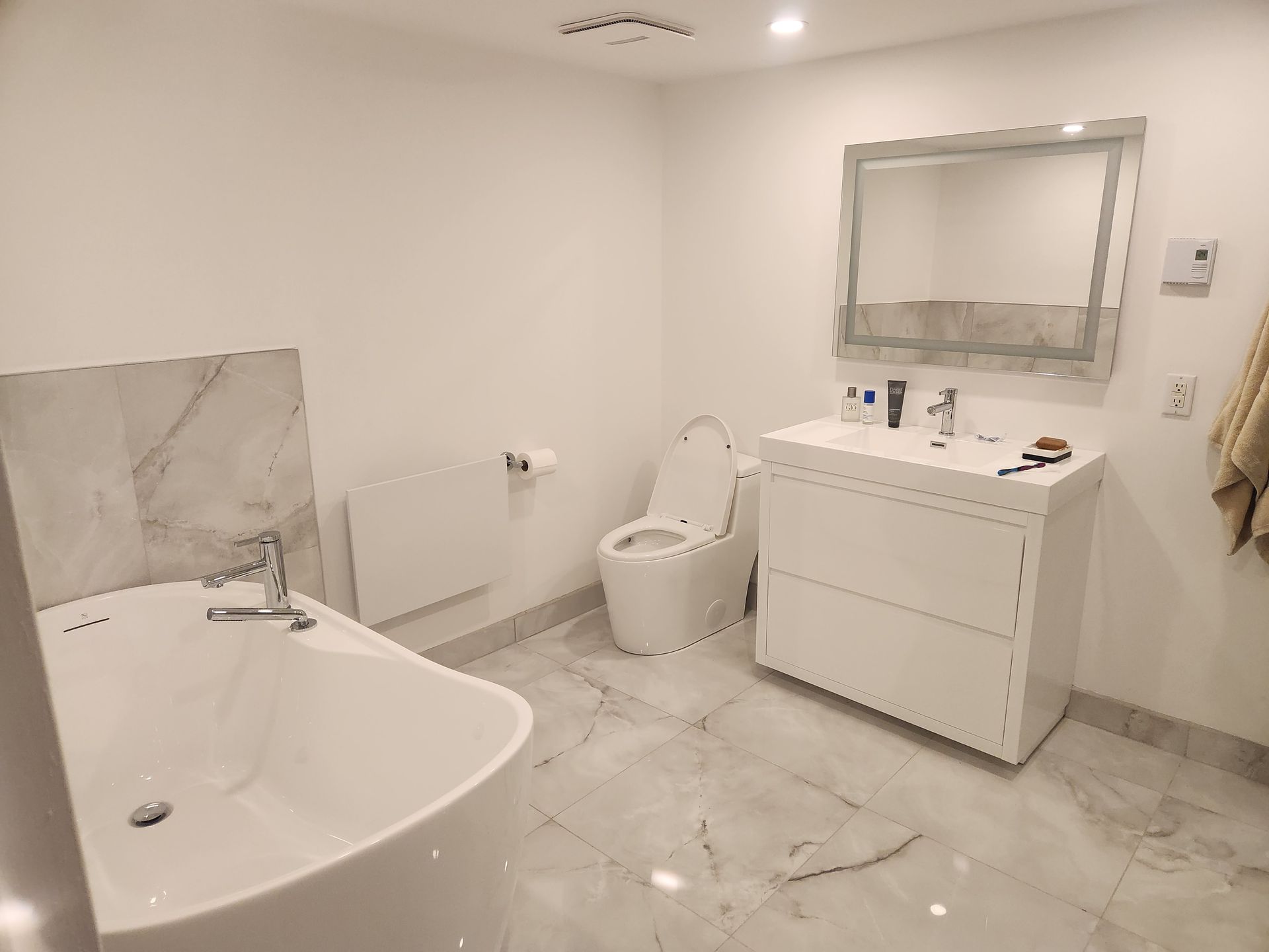 Salle de bain blanche avec baignoire, toilettes, vanité et sols en marbre.