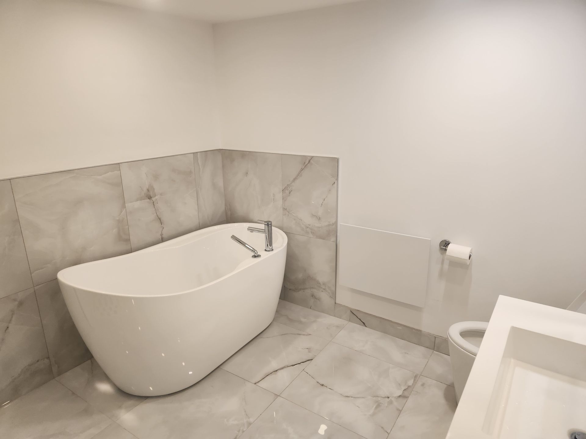 Salle de bain moderne blanche avec baignoire autoportante, carrelage en marbre et toilettes.