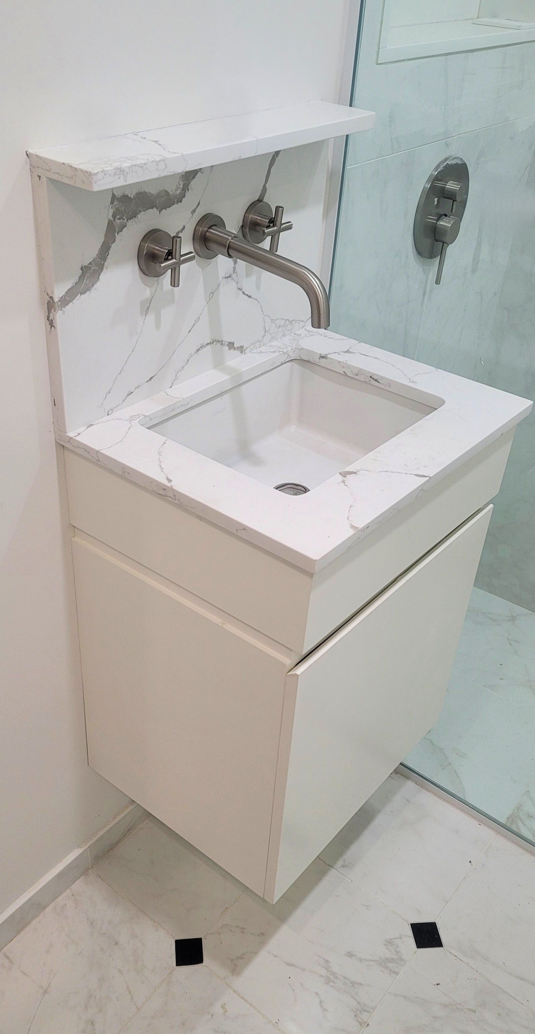 Meuble-lavabo mural blanc avec dosseret en marbre et comptoir en quartz; un lavabo blanc et un robinet en nickel poli.