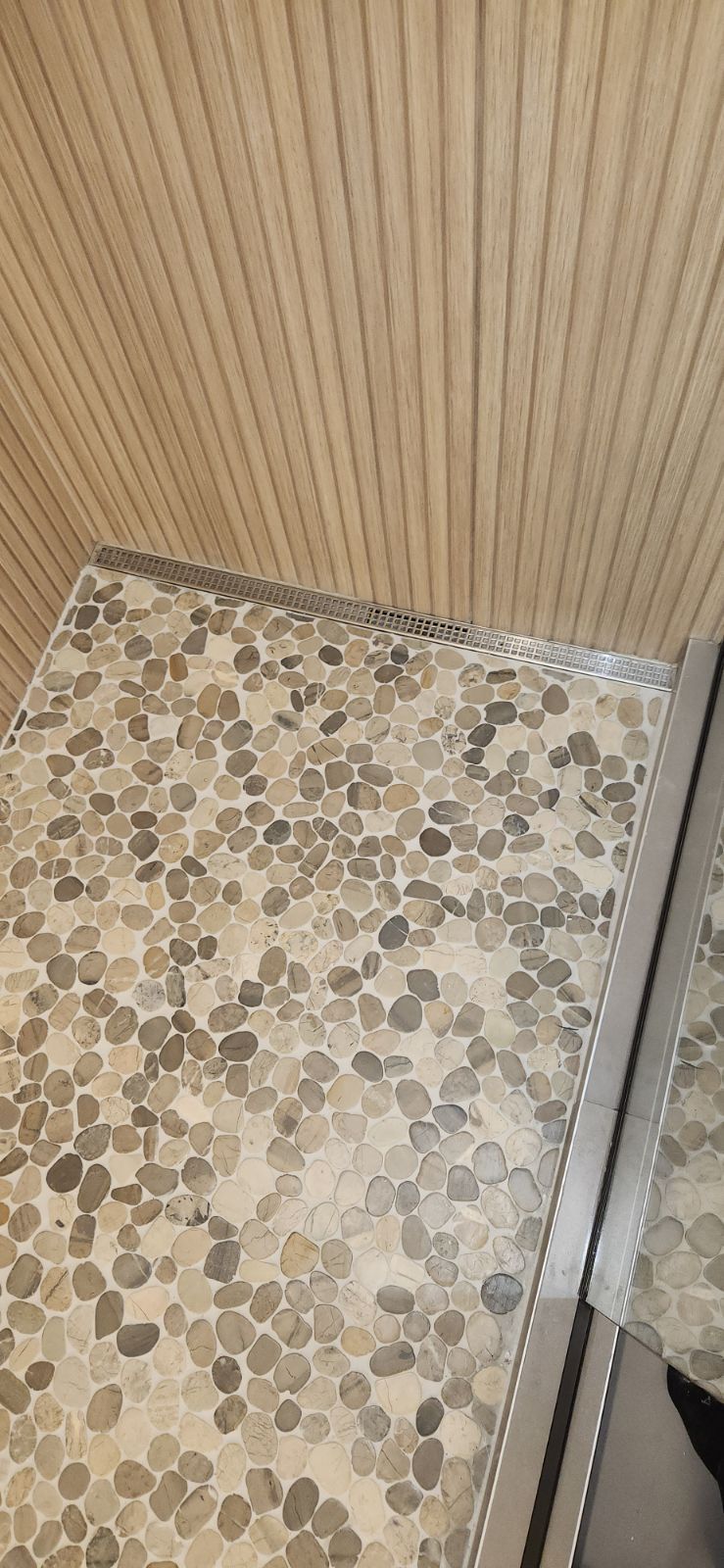 Gros plan d'un sol de douche avec de petits carreaux arrondis et gris à côté d'un mur en bois.
