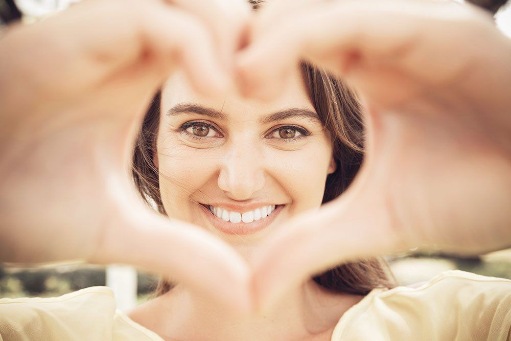 Woman smiling with perfect teeth making a heart shape with her hands