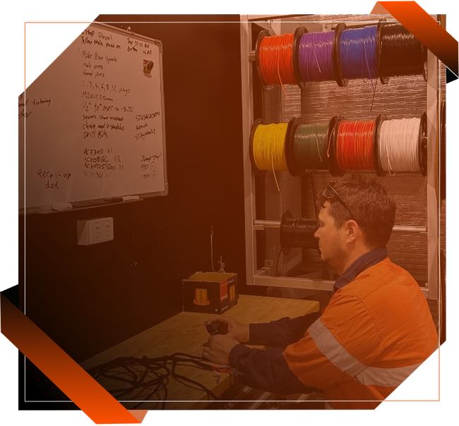 A man is sitting at a desk in front of a white board with spools of wires on it.