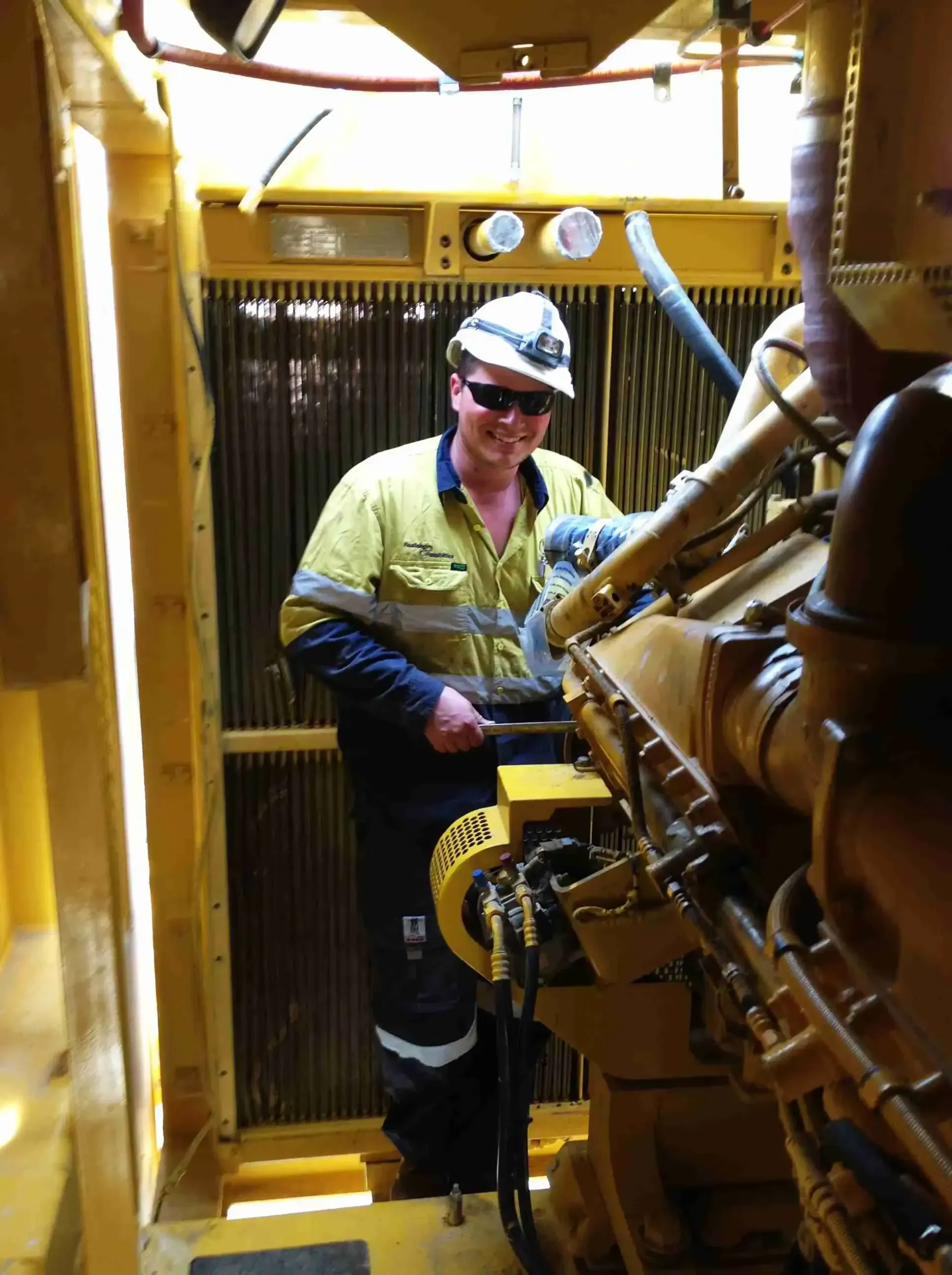 A man wearing a hard hat and sunglasses is working on a machine