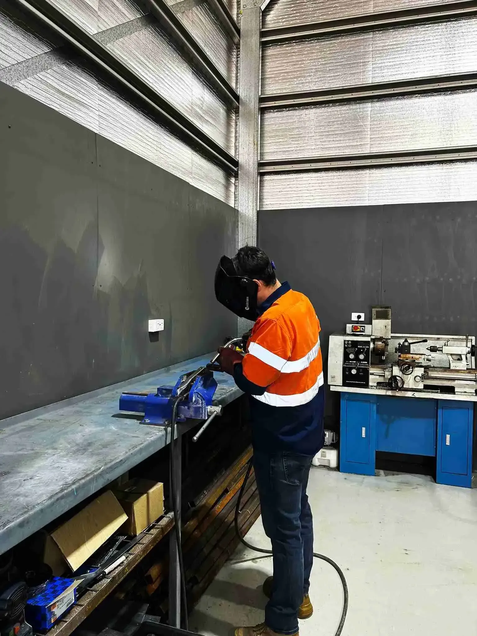 A man wearing a welding helmet is working on a machine in a factory.