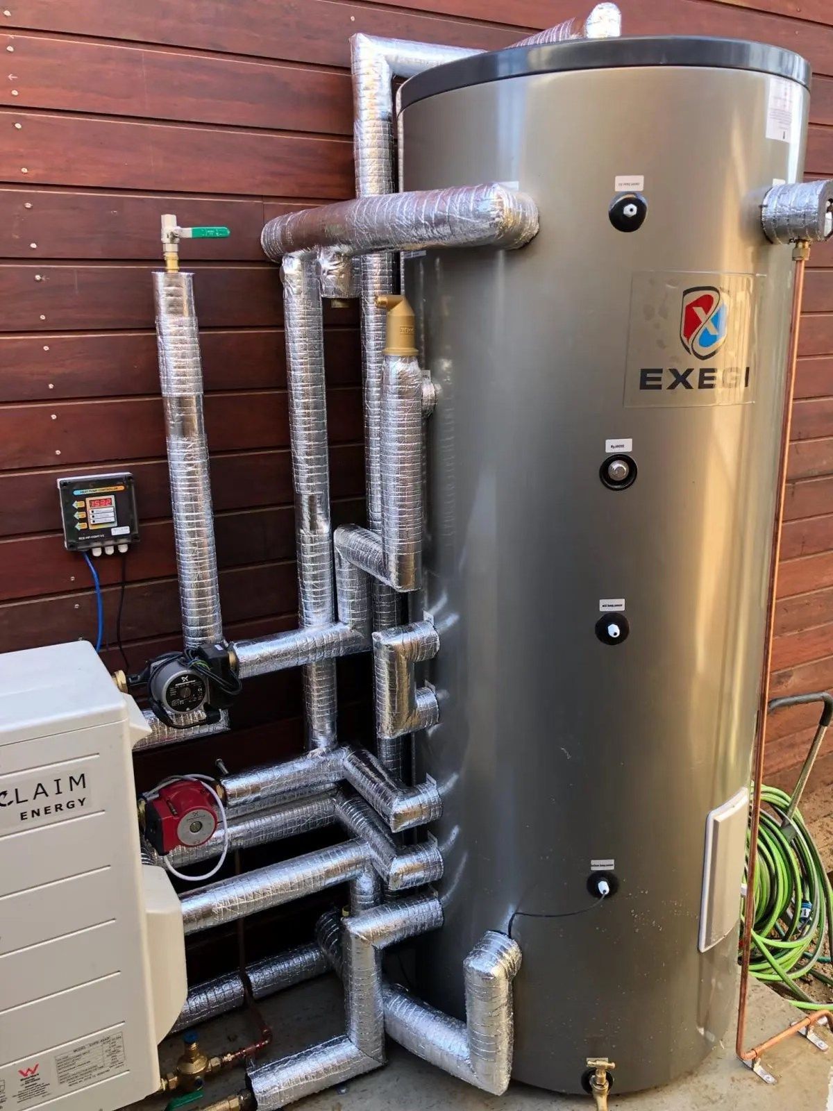 Outdoor stainless-steel hot water tank with insulated pipes beside a wooden fence — Southern Trade Services in Warburton, VIC