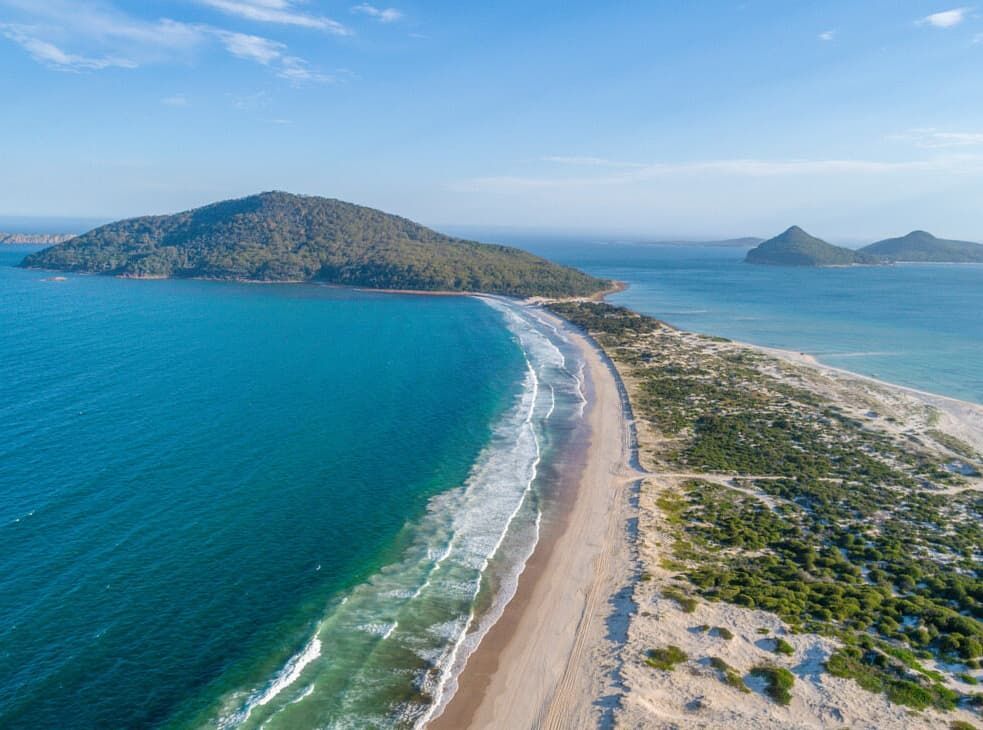 An Aerial View Of A Beach And Ocean With A Small Island In The Distance — Penman Projects In Nelson Bay, NSW