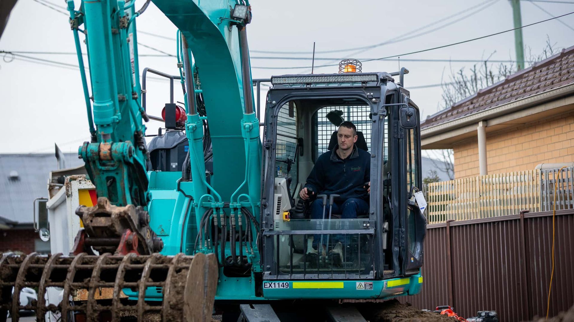A Man Is Driving An Excavator On A Construction Site — Frank Plumbing In Delacombe, VIC