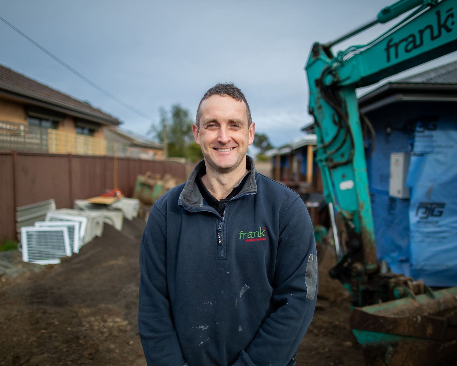 A man is standing in front of a green excavator — Frank Plumbing In Delacombe, VIC