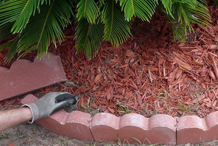 A Person Wearing a Glove is Laying a Brick Edging in a Garden — Tallow Tree Services Pty Ltd in Evans Head, NSW