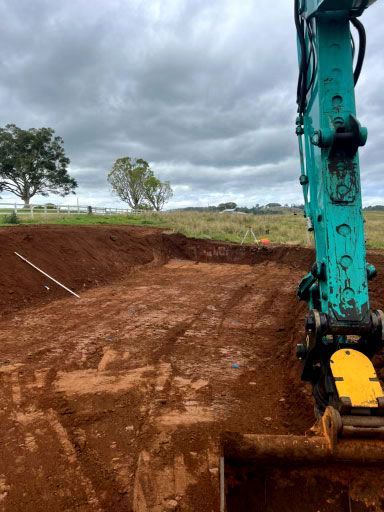 A Blue Excavator is Digging a Hole in the Dirt in a Field — Tallow Tree Services Pty Ltd in Bangalow, NSW